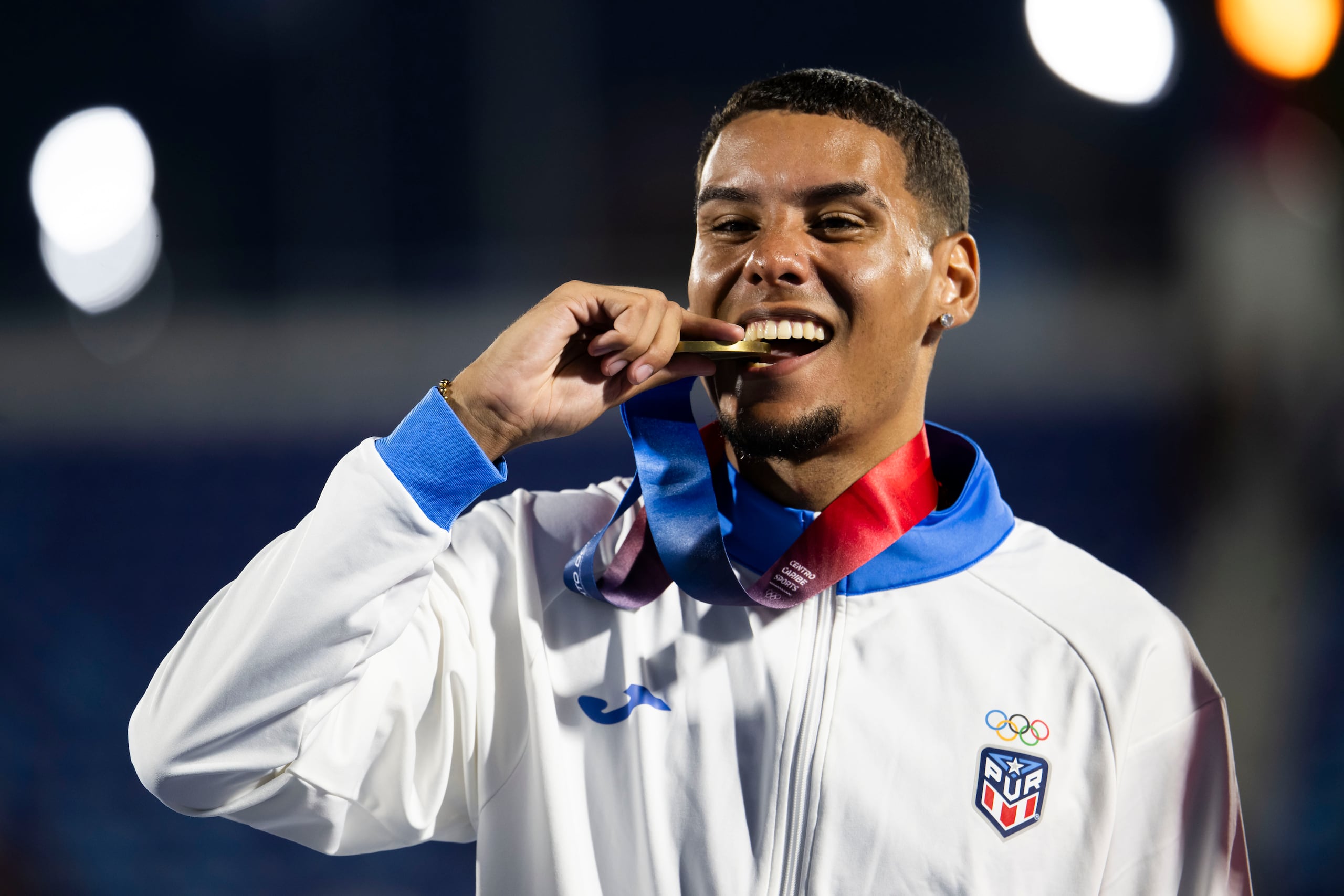 José Figueroa muerde la medalla de oro que ganó en los 200 metros de los Juegos Centroamericanos y del Caribe Santo Domingo 2026.
