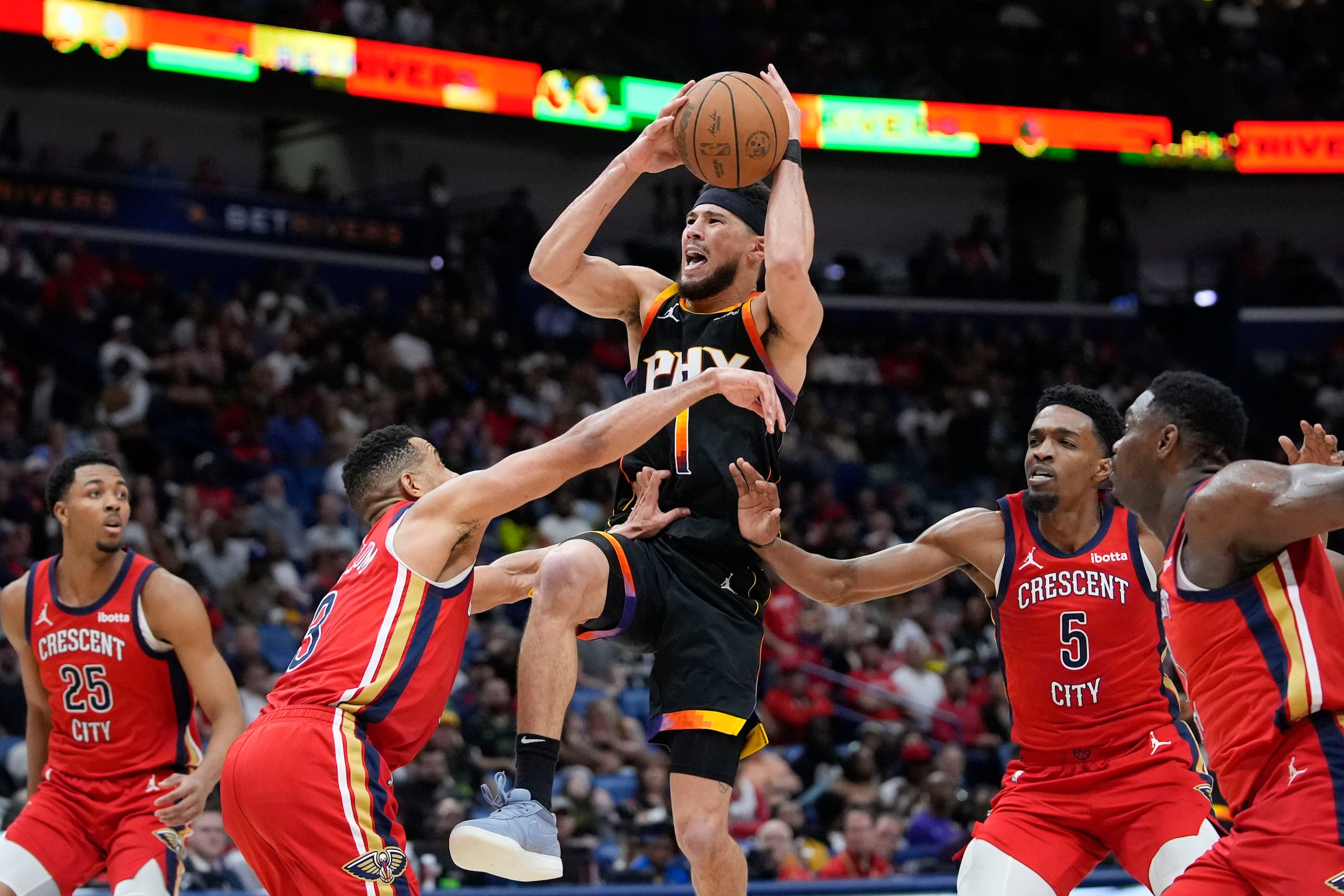 Devin Booker, de los Suns de Phoenix, ataca el canasto ante CJ McCollum (3) Herbert Jones (5), de los Pelicans de Nueva Orleans.