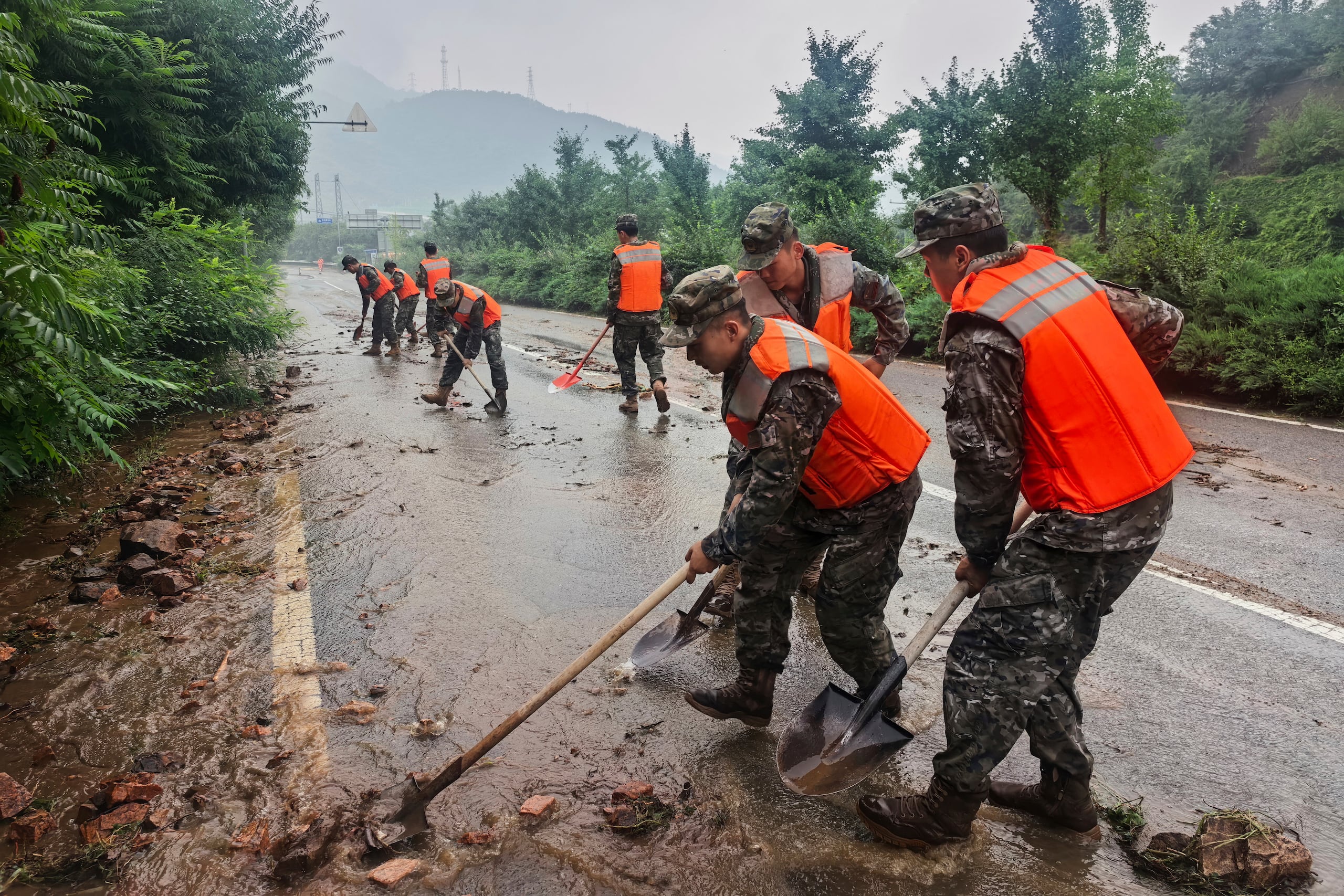 En esta imagen publicada por la agencia de noticias Xinhua, miembros de la Policía Armada Popular China ayudan a despejar un tramo de carretera en el distrito de Miyun, duraante alertas de lluvias, al norte de Beijing, el 27 de julio de 2025. (Wang Xiqing/Xinhua via AP)