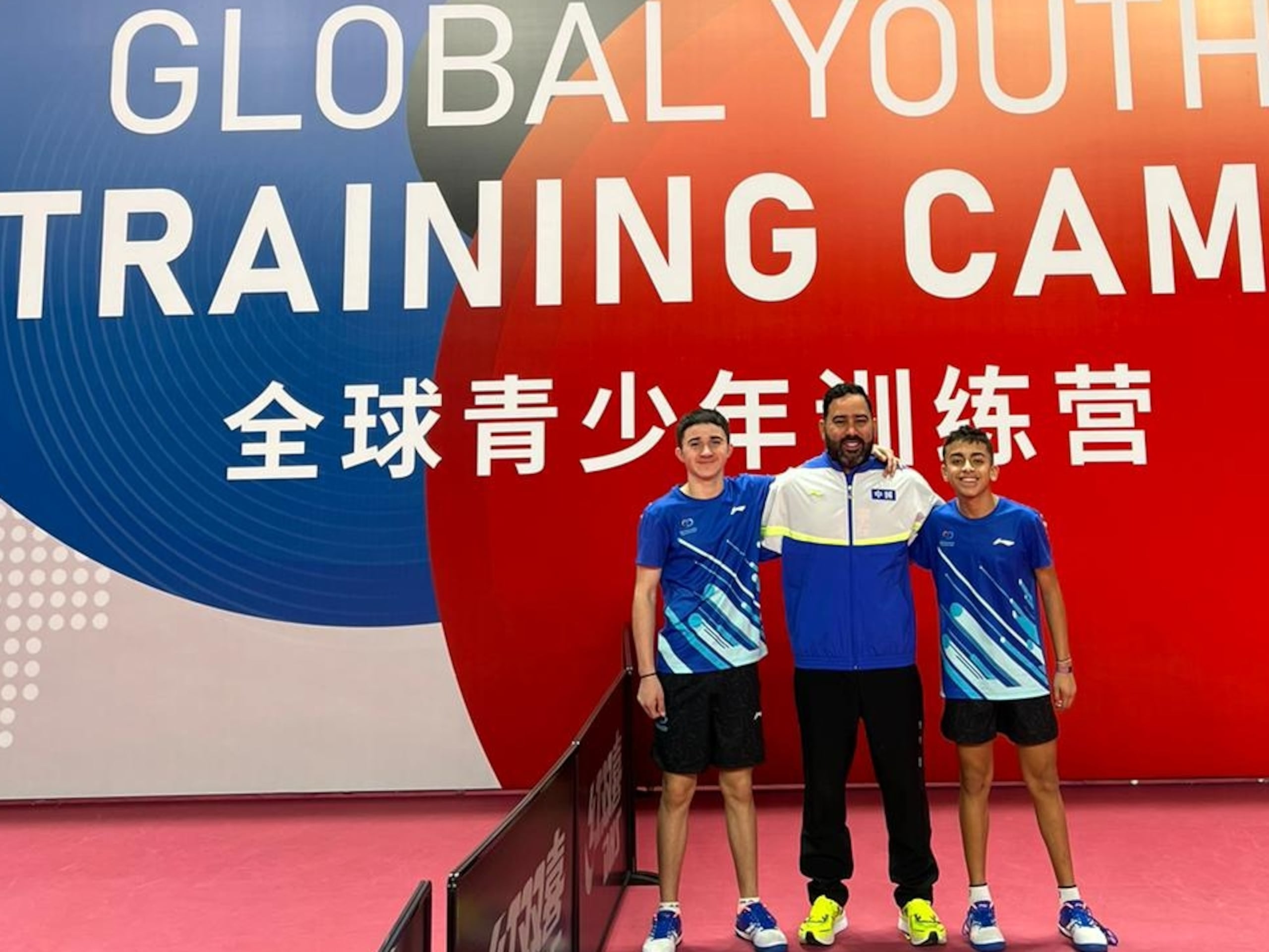 Enrique Ríos, el entrenador Edgardo Vázquez y Steven Morero posan en China frente al cartel de campamento que realizan en ese país.