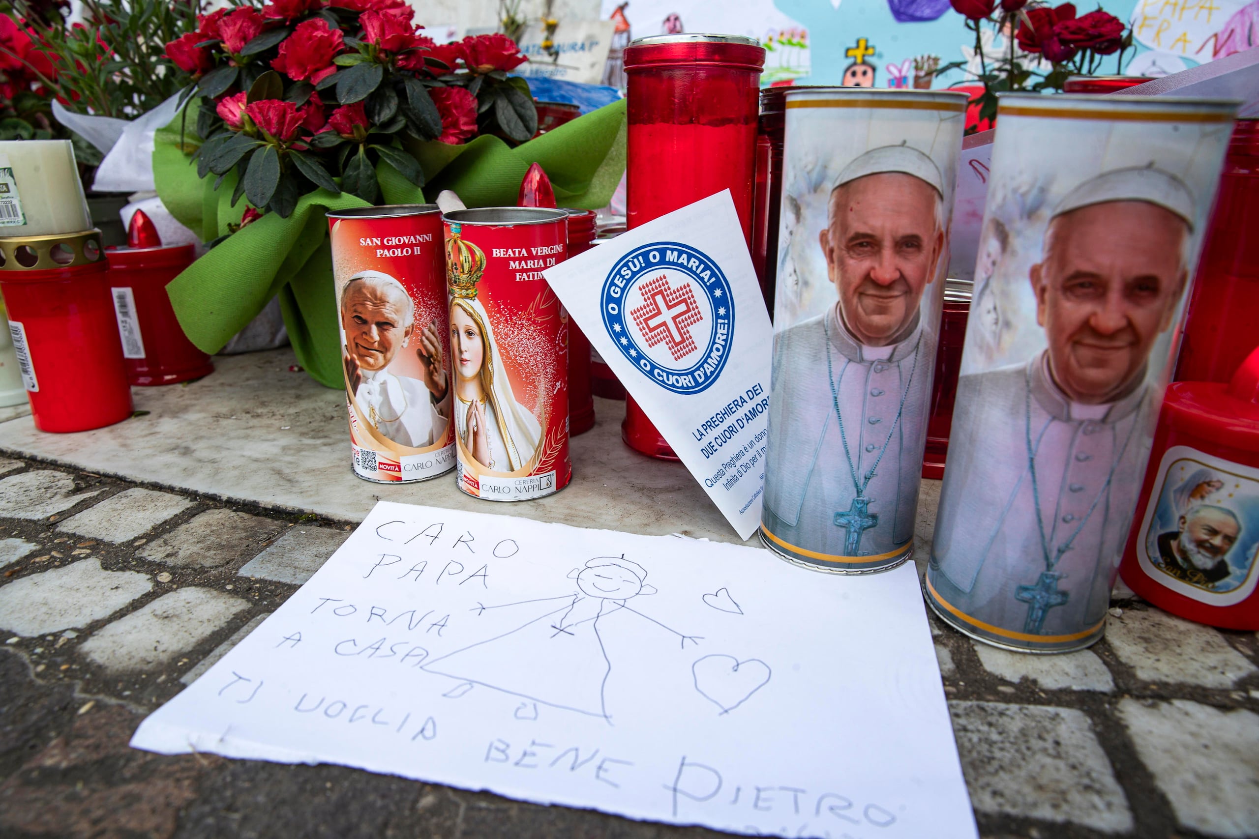 Velas y mensajes están expuestos bajo la estatua de Juan Pablo II en la entrada del Hospital Gemelli, donde está hospitalizado el papa Francisco.