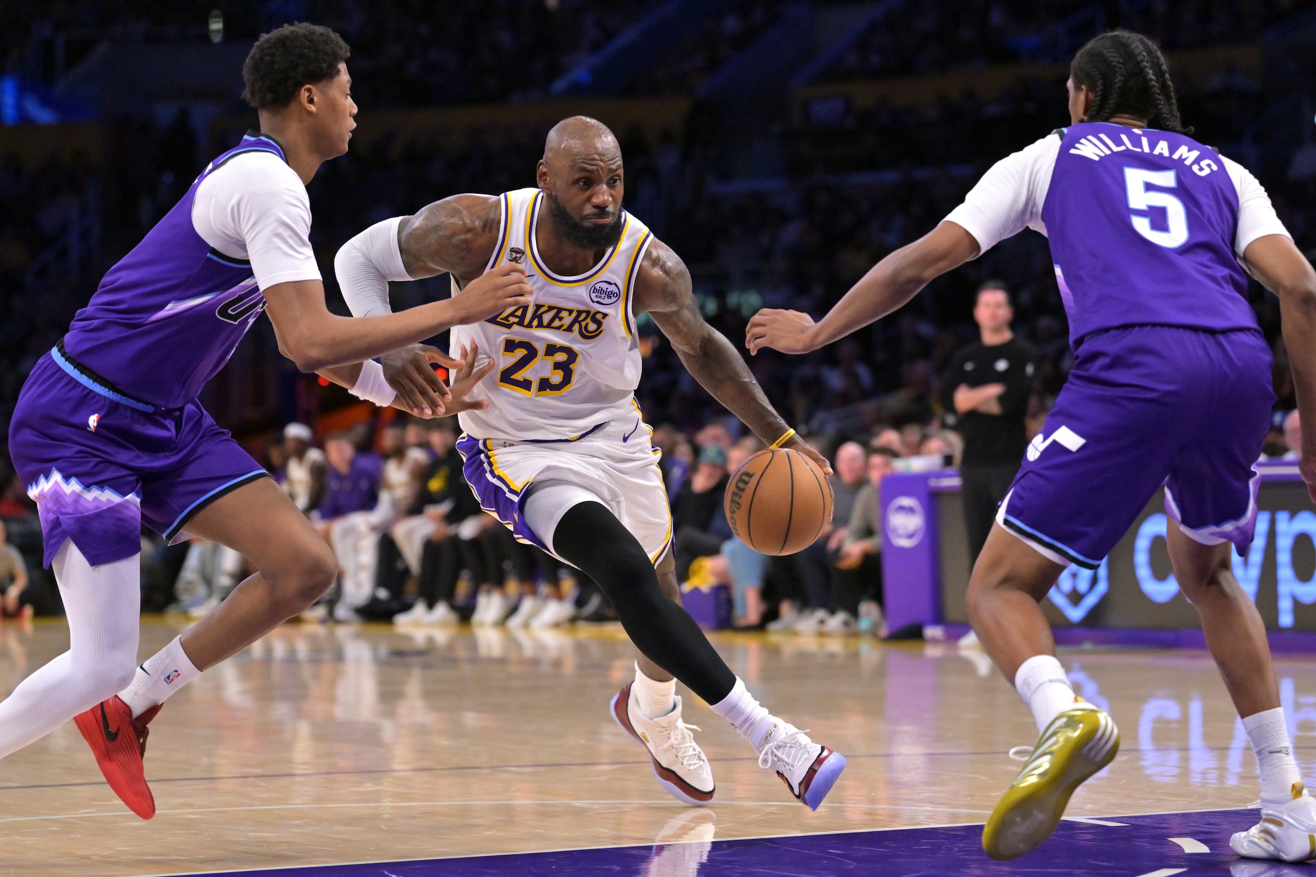 LeBron James (23), de los Lakers de Los Ángeles, lleva el balón entre Ace Bailey, izquierda, y Cody Williams, del Jazz de Utah, durante la primera mitad del juego de baloncesto de la NBA el domingo 12 de abril de 2026, en Los Ángeles. (AP Foto/Jayne Kamin-Oncea)