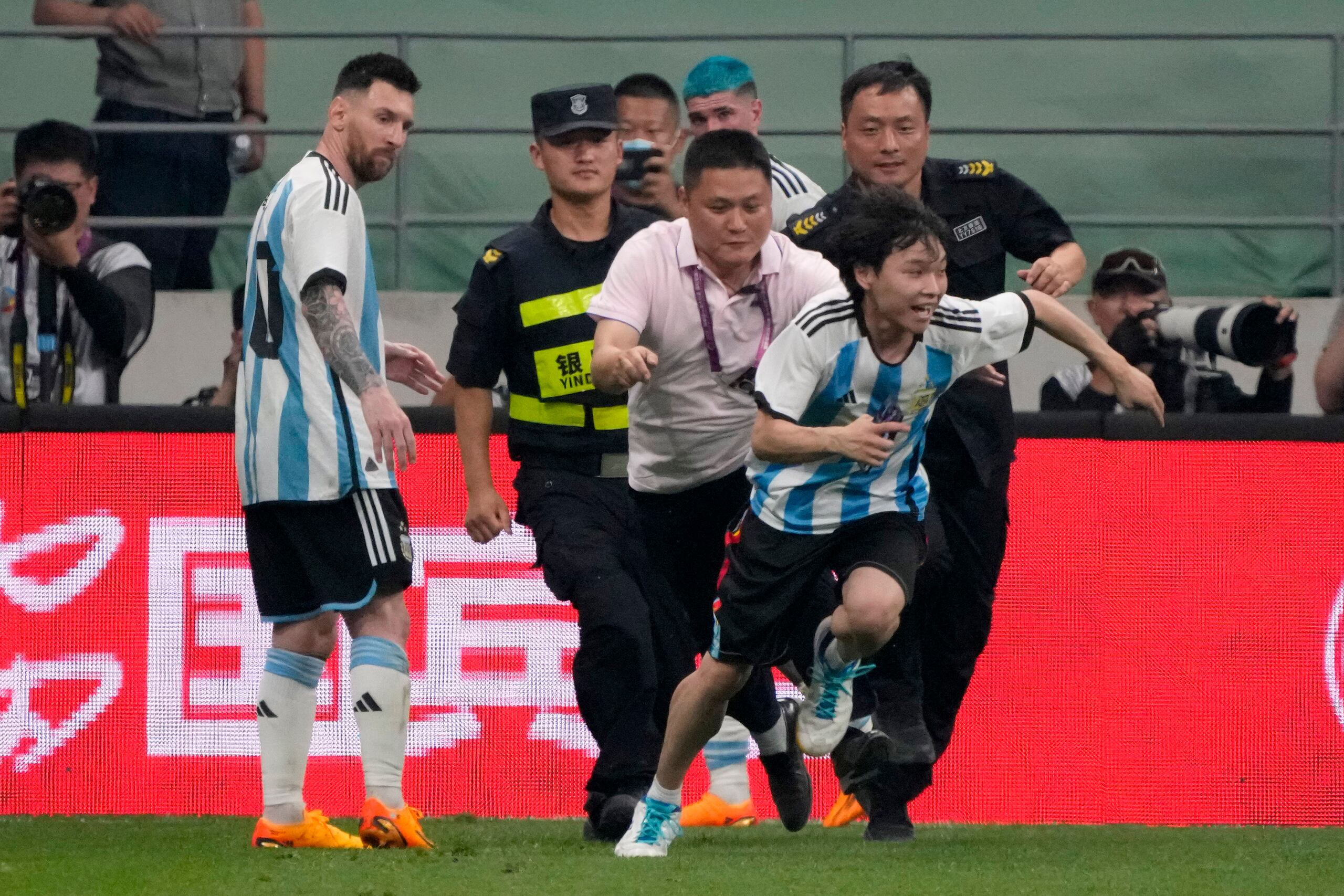 El delantero argentino Lionel Messi (izquierda) observa cuando la seguridad persigue a un aficionado durante un partido amistoso, el jueves 15 de junio de 2023, en Beijing. (AP Foto/Mark Schiefelbein)