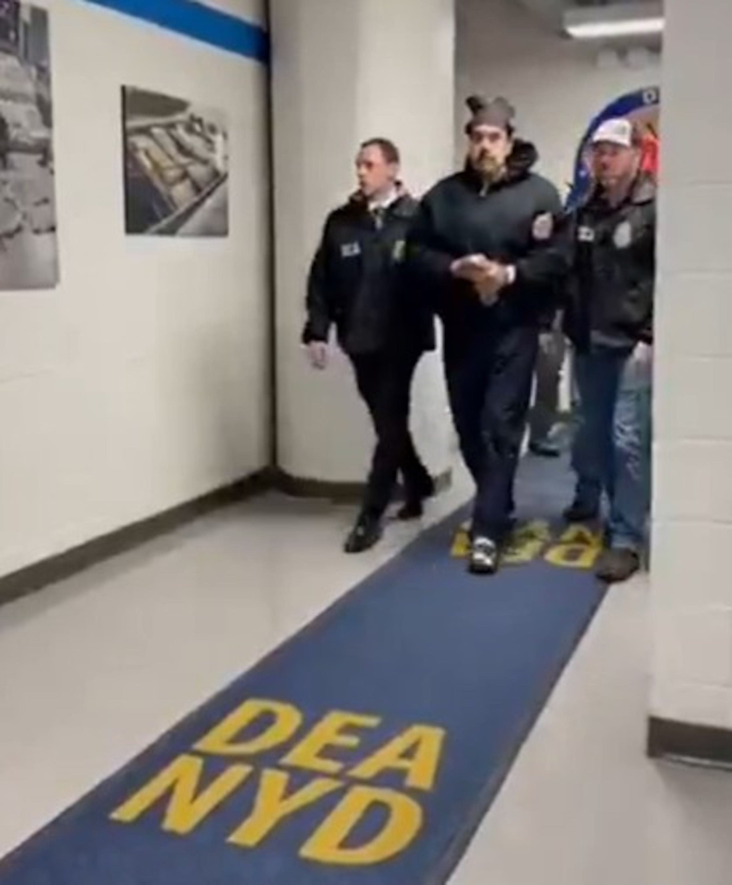 En el video se ve a Maduro con una sudadera negra con capucha, caminando por un pasillo con una alfombra azul que lleva la inscripción “DEA NYD”.