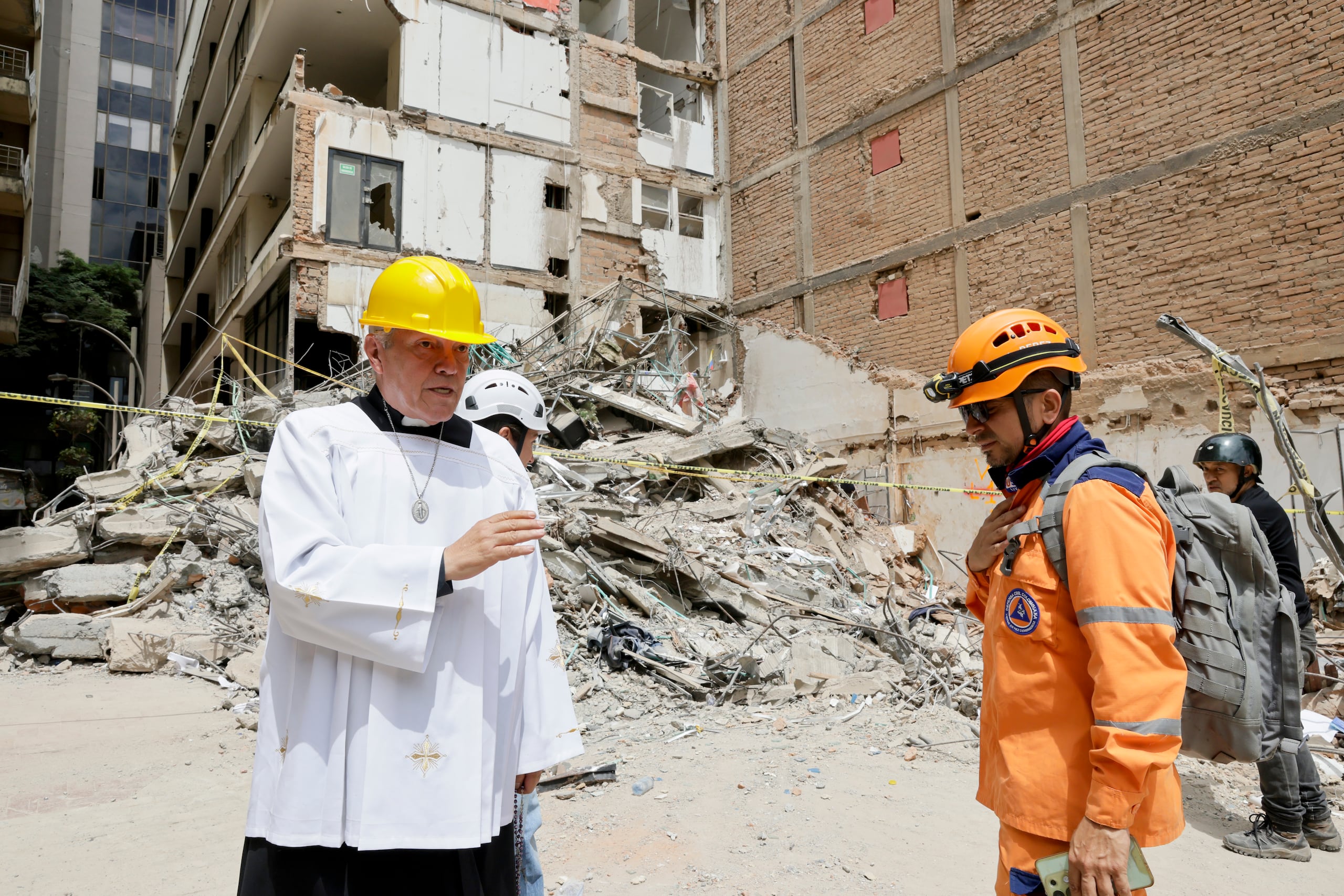 El padre Nelson Giraldo Mejía (i) ora por las víctimas del terremoto de magnitud 7.4 ocurrido el pasado lunes, frente a los escombros del edificio Santiago Londoño, con una réplica de la Virgen de Nuestra Señora de la Pobreza, este 14 de agosto de 2026, en Pereira, Colombia. (EFE/ Carlos Ortega)