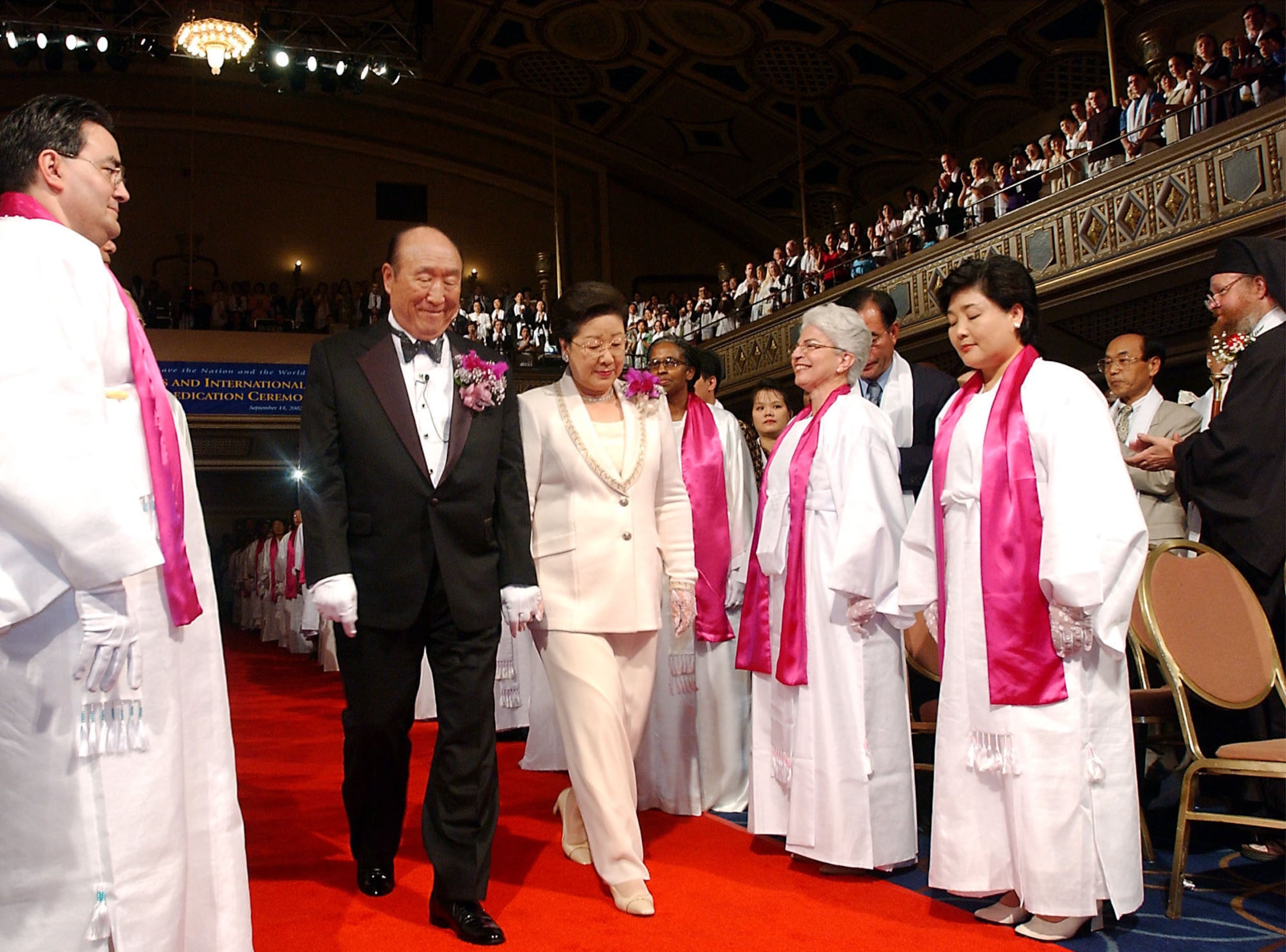 El reverendo y la señora Sun Myung Moon caminan por una alfombra roja mientras son presentados durante la parte de Confirmación de Votos de la Ceremonia de Bendición y Reafirmación de Parejas Interreligiosas e Internacionales, el 14 de septiembre de 2002 en el Manhattan Center de Nueva York. Unas 500-600 parejas participaron en la ceremonia de Nueva York, y se estimaba que 21 millones de parejas lo hicieron en todo el mundo a través de una transmisión simultánea a 185 países.