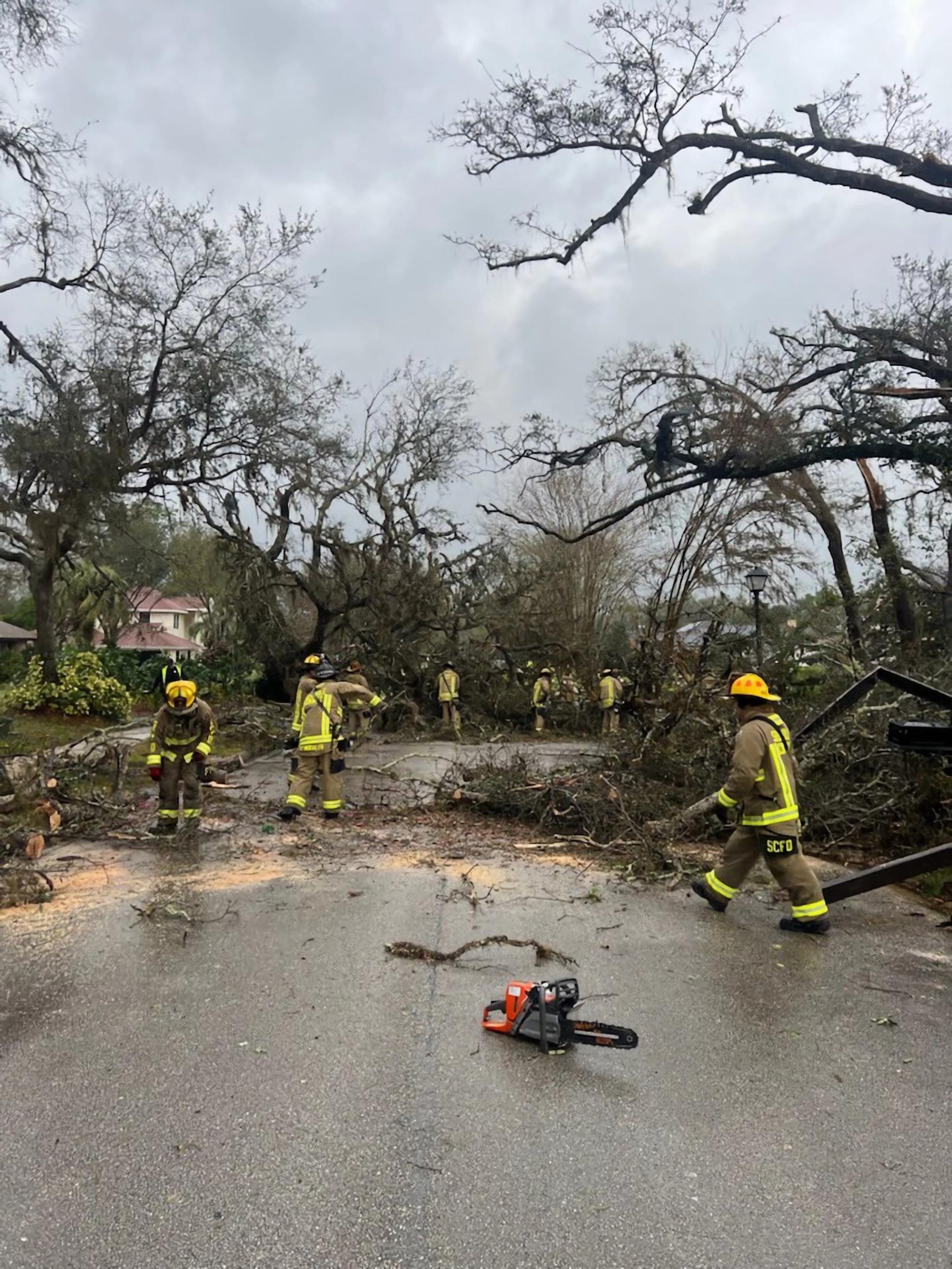 Fotografía cedida por el Departamento de Bomberos del Condado Seminole donde aparece unos agentes mientras retiran los escombros y arbustos de una carretera el lunes en Longwood, Florida.