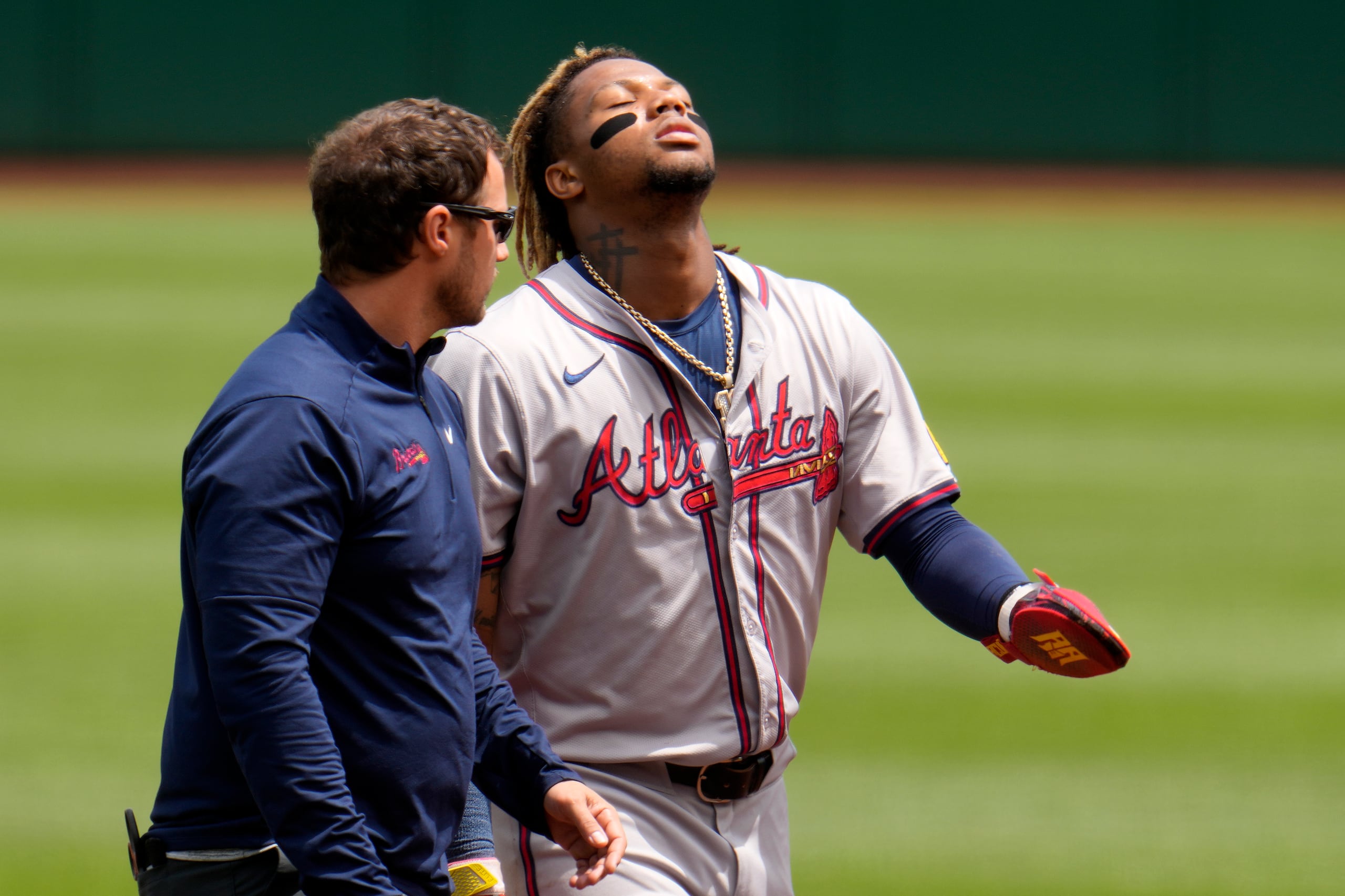 Ronald Acuña Jr., derecha, de los Bravos de Atlanta, camina para abandonar el campo acompañado del asistente médico después de sufrir una lesión al intentar robarse tercera durante la primera entrada del juego de béisbol en contra de los Piratas de Pittsburgh, el domingo 26 de mayo de 2024, en Pittsburgh. (AP Foto/Gene J. Puskar)