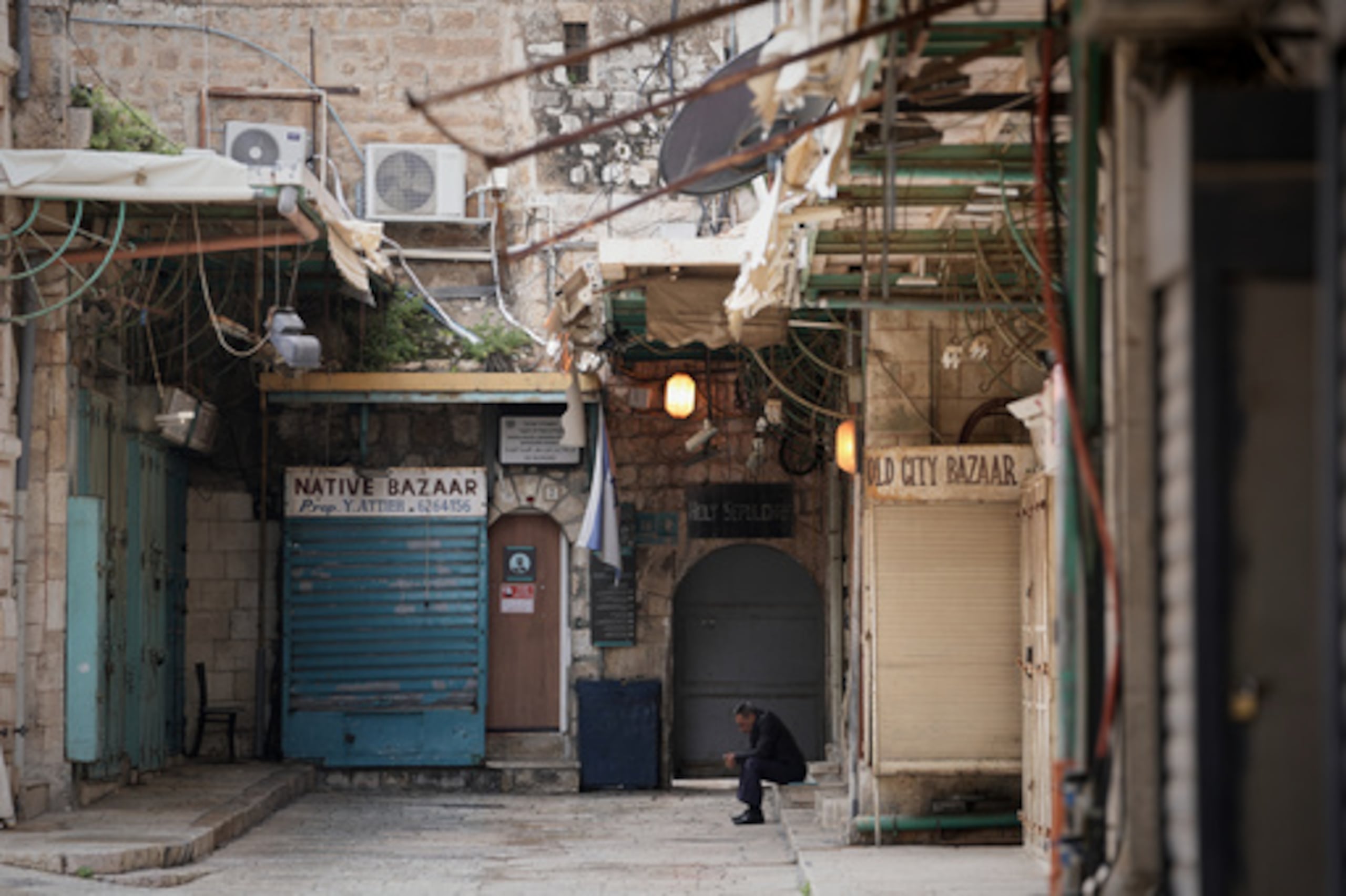 Un hombre sentado junto a una puerta cerrada de la Iglesia del Santo Sepulcro y las tiendas cerradas en la Ciudad Vieja de Jerusalén, que permanece fuera del alcance de los visitantes en medio de la guerra con Irán, el viernes 27 de marzo de 2026. (AP Photo/Mahmoud Illean)
