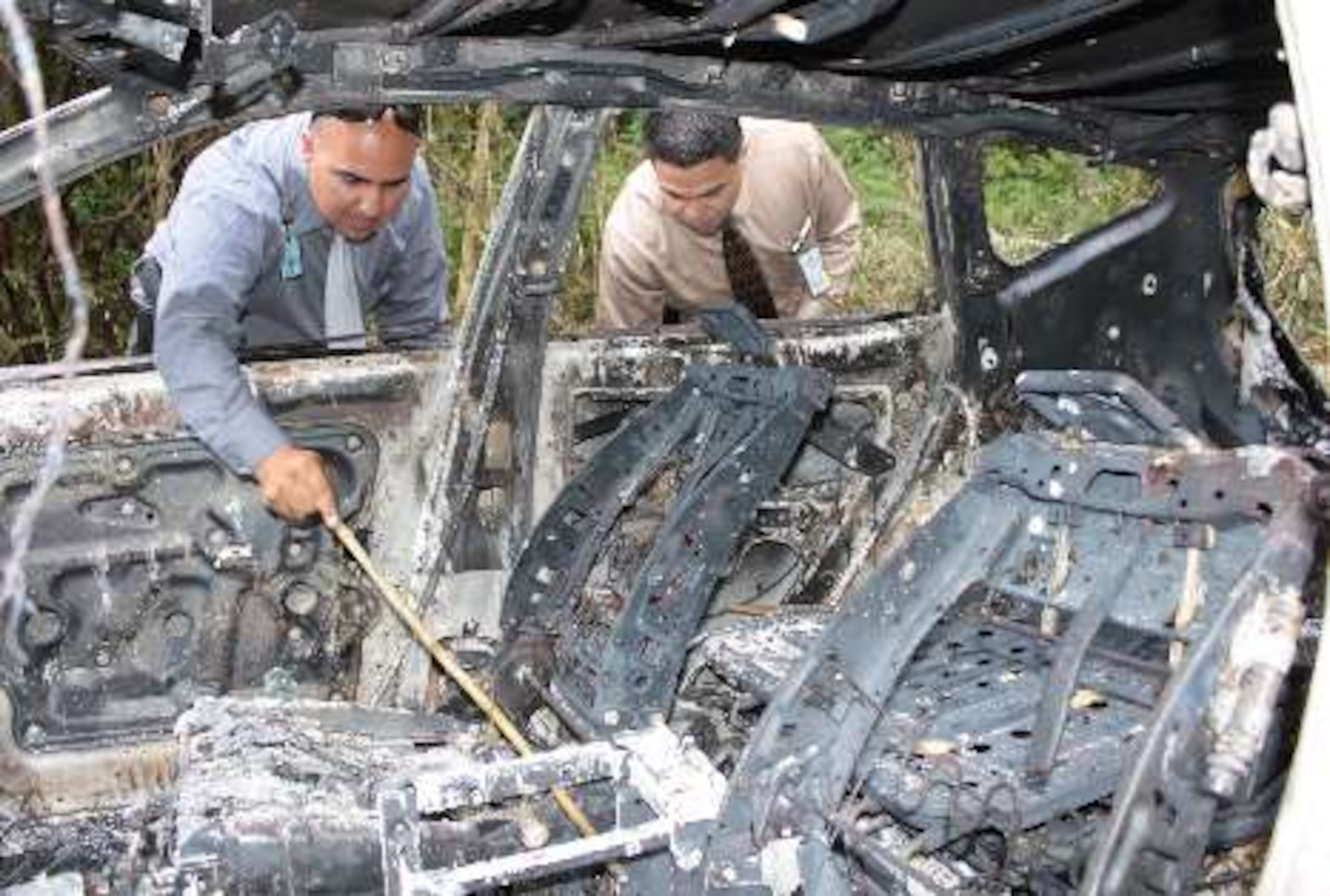Agentes del CIC de Arecibo inspeccionan un vehículo quemado a la orilla de la carretera PR-673 el que está vinculado  aparentemente con el asesinato de Rosado Santana.
