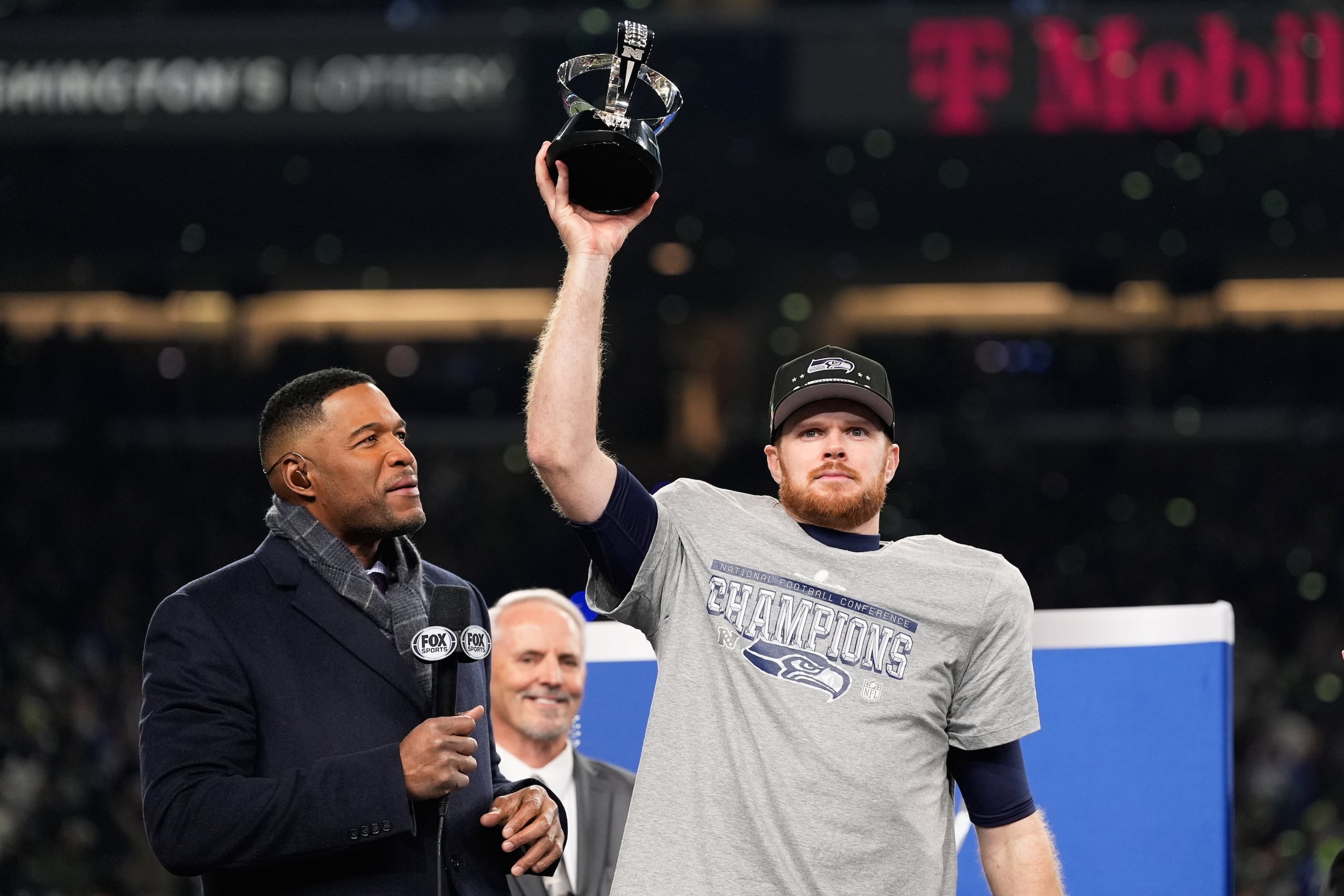El quarterback de los Seahawks de Seattle Sam Darnold levanta el trofeo de campeón de la NFC junto al comentarista y exjugador Michael Strahan tras vencer a los Rams de Los Ángeles el domingo 25 de enero del 2026. (AP Foto/Godofredo A. Vásquez)