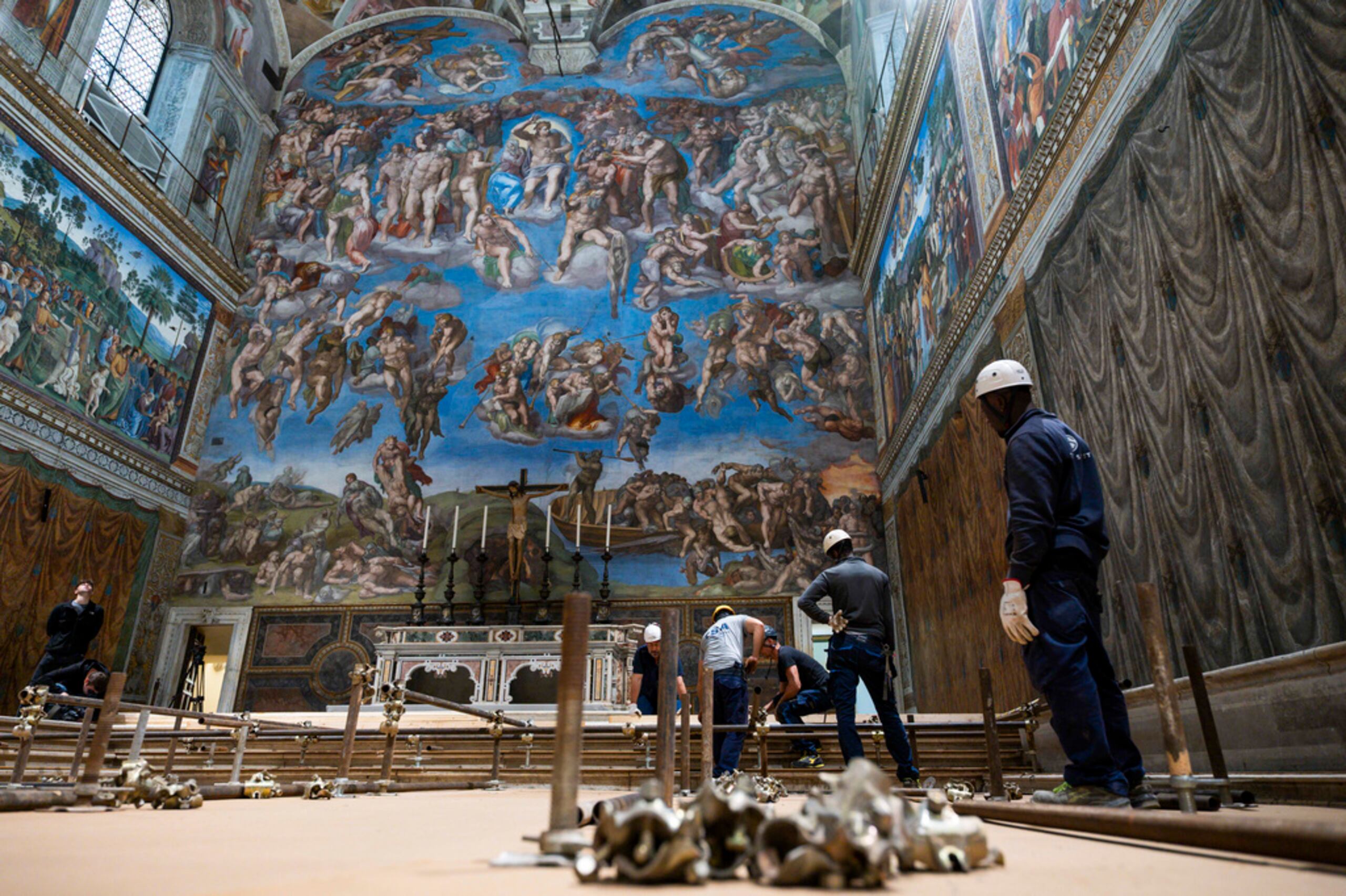 En esta imagen del lunes 28 de abril de 2025, varios trabajadores preparan la capilla Sixtina en el Vaticano, donde comenzará el próximo cónclave el 7 de mayo, ante el fresco de Miguel Ángel "El juicio final".