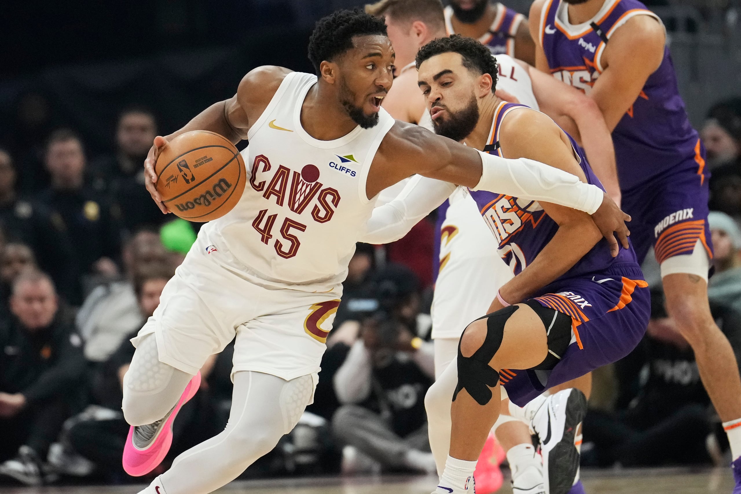 El escolta de los Cavaliers de Cleveland, Donovan Mitchell (45), conduce alrededor del escolta de los Suns de Phoenix, Tyus Jones, al frente a la derecha, en la primera mitad de un partido de baloncesto de la NBA.
