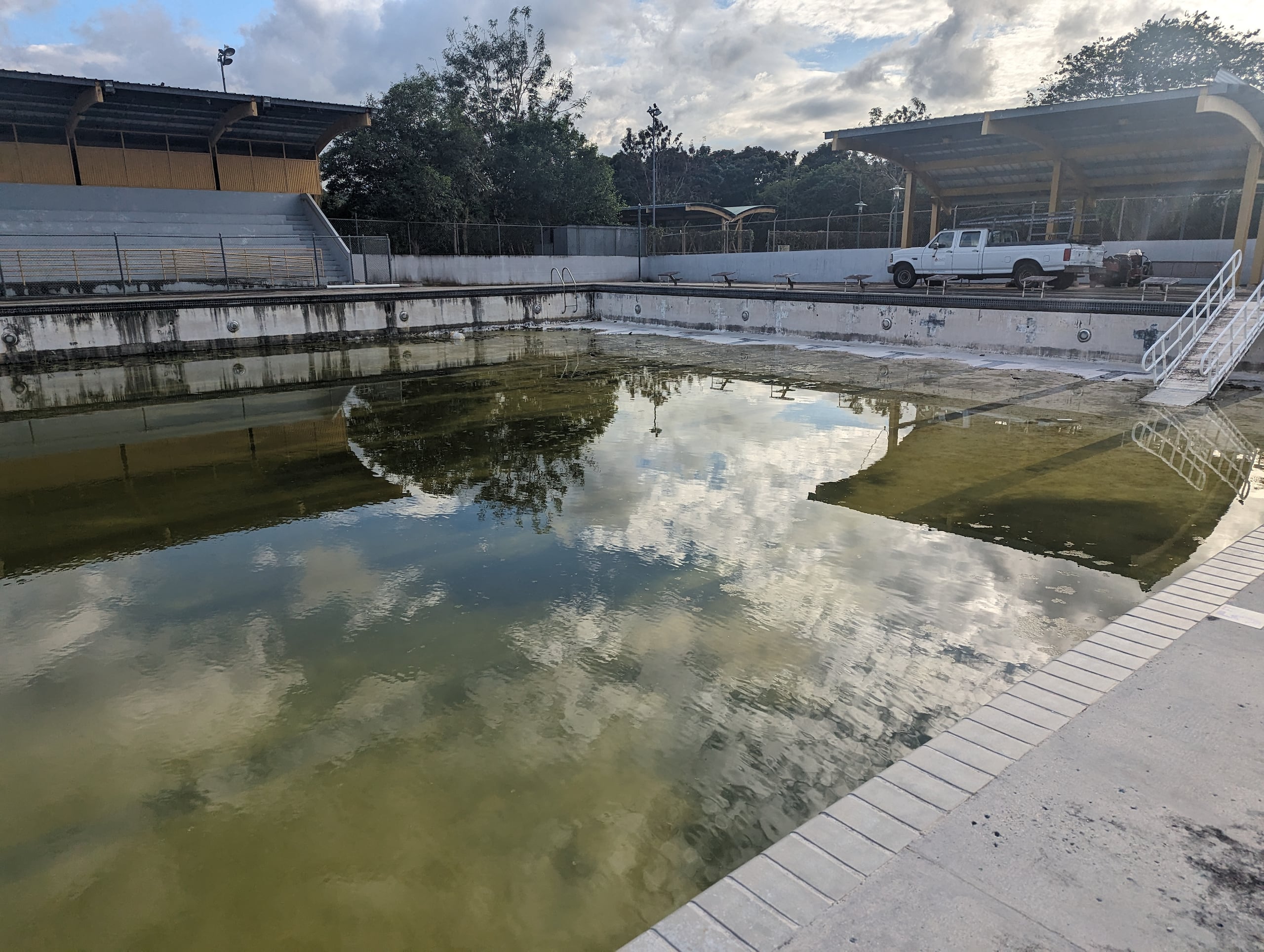 Agua con hongo verde adorna el estanque mientras un puñado de vehículos del Gobierno sirven de vigilantes dentro del desolado espacio.