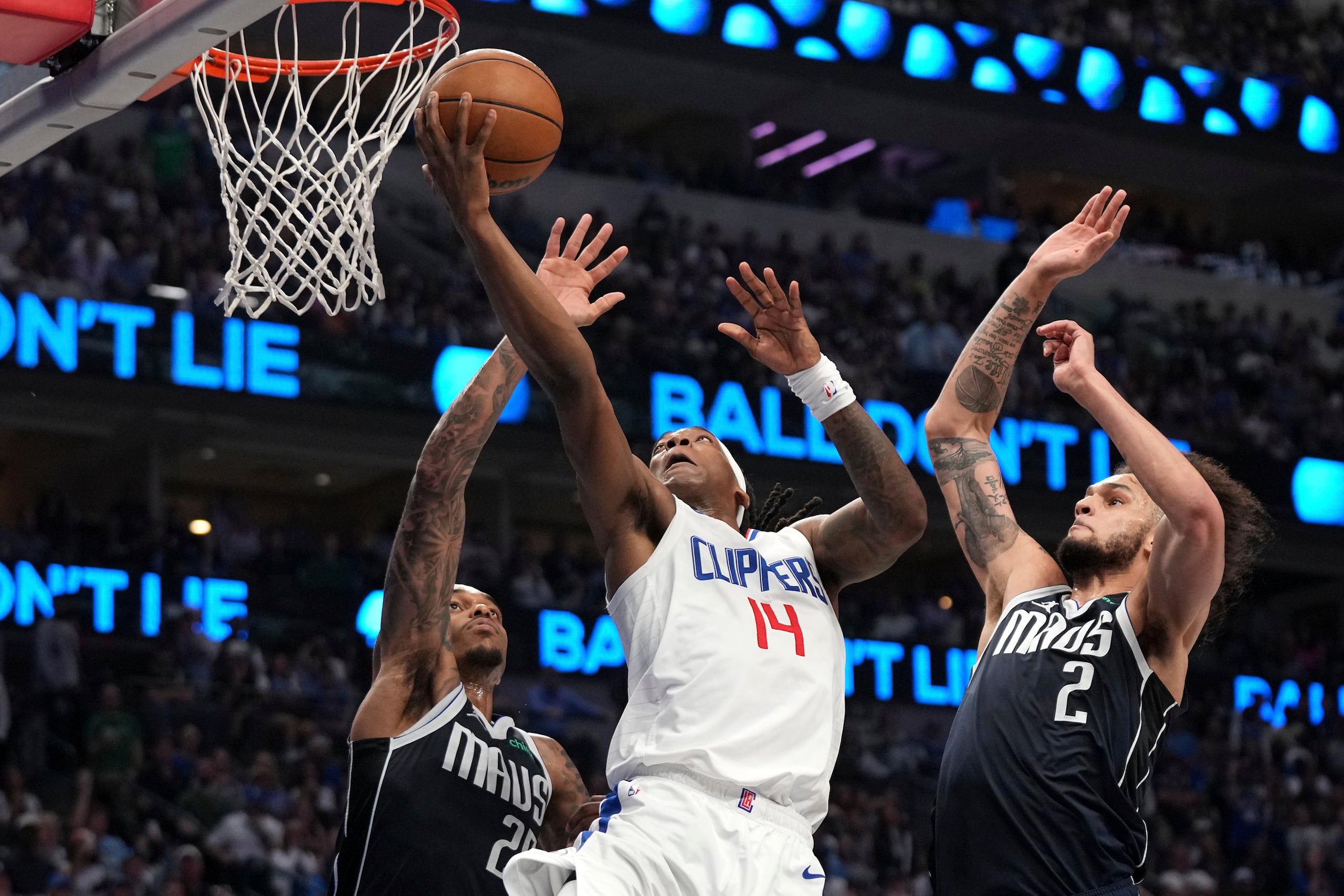 El base de los Clippers de Los Ángeles Terance Mann salta con el balón para anotar frente al alero P.J. Washington y el pívot Dereck Lively II de los Mavericks de Dallas en la serie de primera ronda de la postemporada el domingo 28 de abril del 2024. (AP Foto/Jeffrey McWhorter)