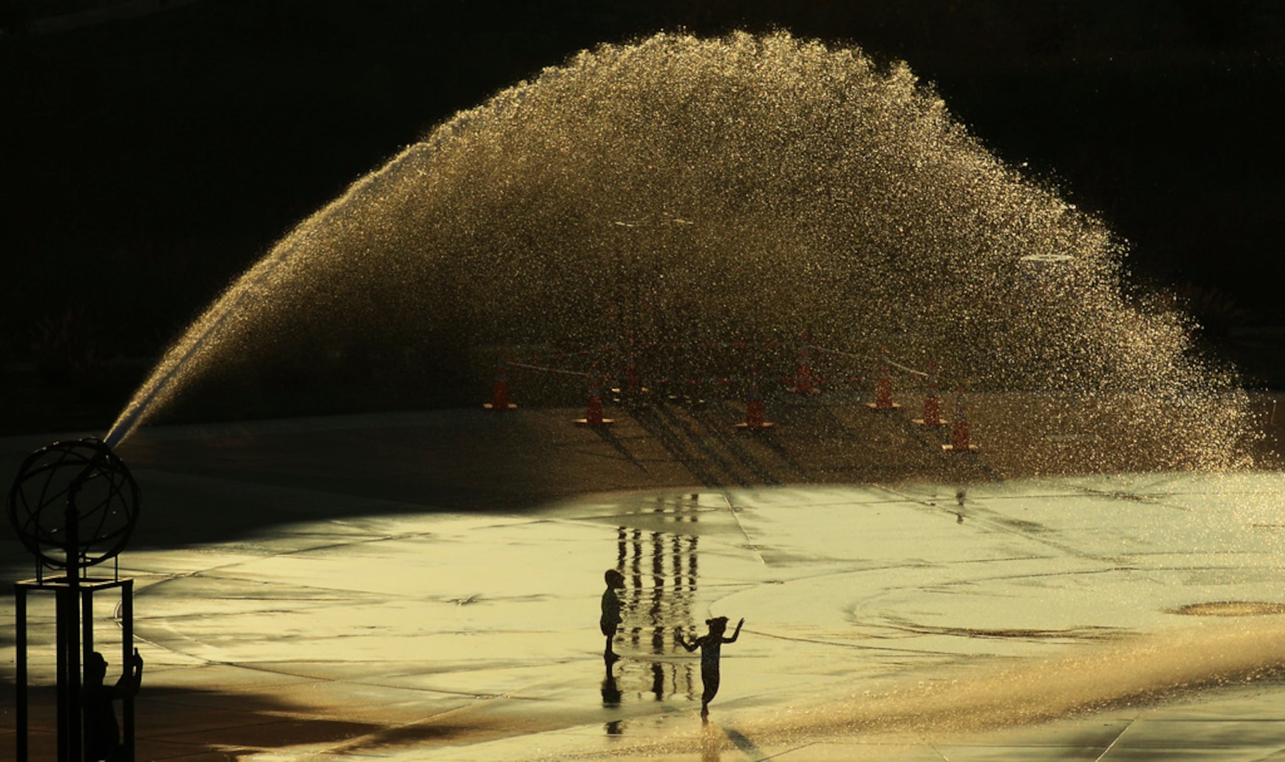 Niños corren a través de la fuente Whirlpool Compass mientras el sol se pone durante una ola de calor el 26 de agosto de 2024, en St. Joseph, Michigan.