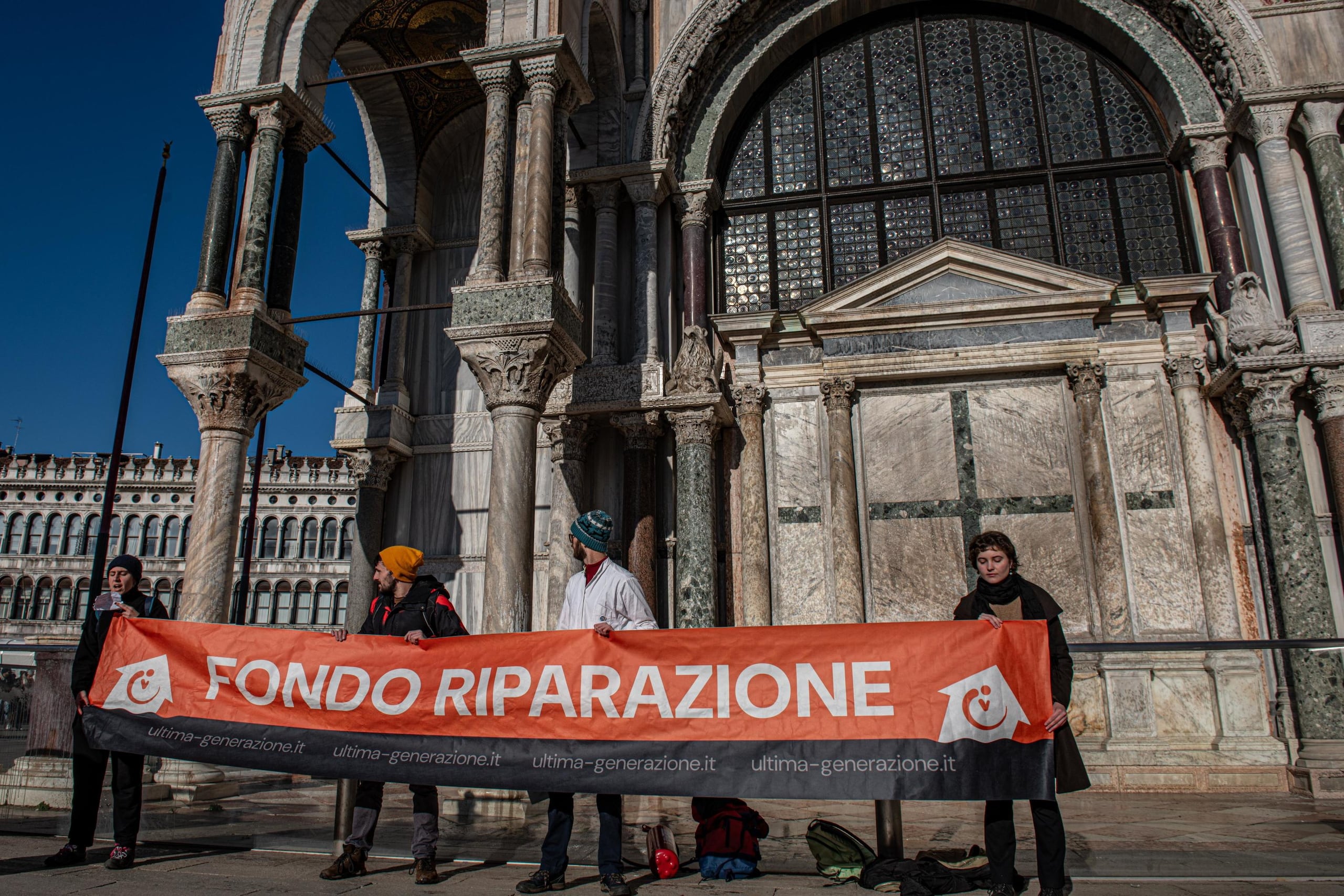 Activistas climáticos sostienen una pancarta después de rociar barro en el exterior de la Basílica de San Marcos durante una protesta en Venecia, Italia, el 7 de diciembre de 2023. Los manifestantes utilizaron extintores para rociar barro líquido en la iglesia paredes, antes de desplegar una pancarta que decía "fondo de reparación". (Protestas, Italia, Niza, Venecia) (EFE/EPA/EDOARDO FIORETTO)