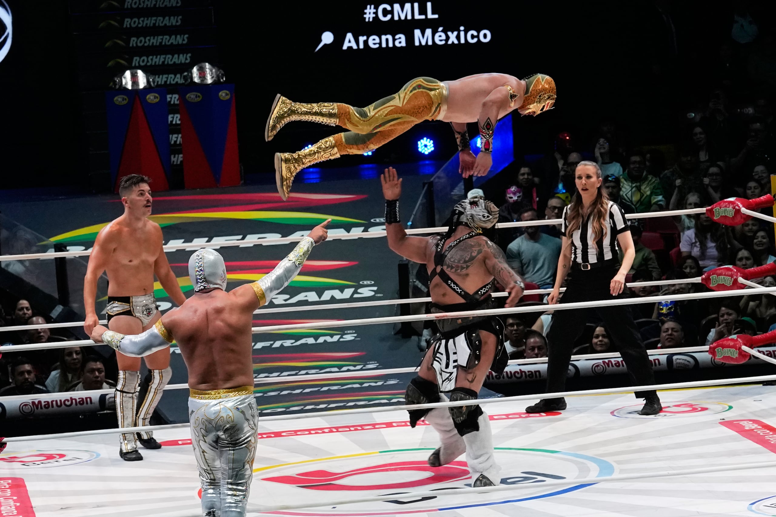 El luchador Máscara Dorada vuela sobre The Beast Mortos, mientras Sammy Guevara (izquierda) y Místico (de espaldas), se enfrentan en el México Arena, en la Ciudad de México, el 26 de junio de 2026. (AP Foto/Marco Ugarte)
