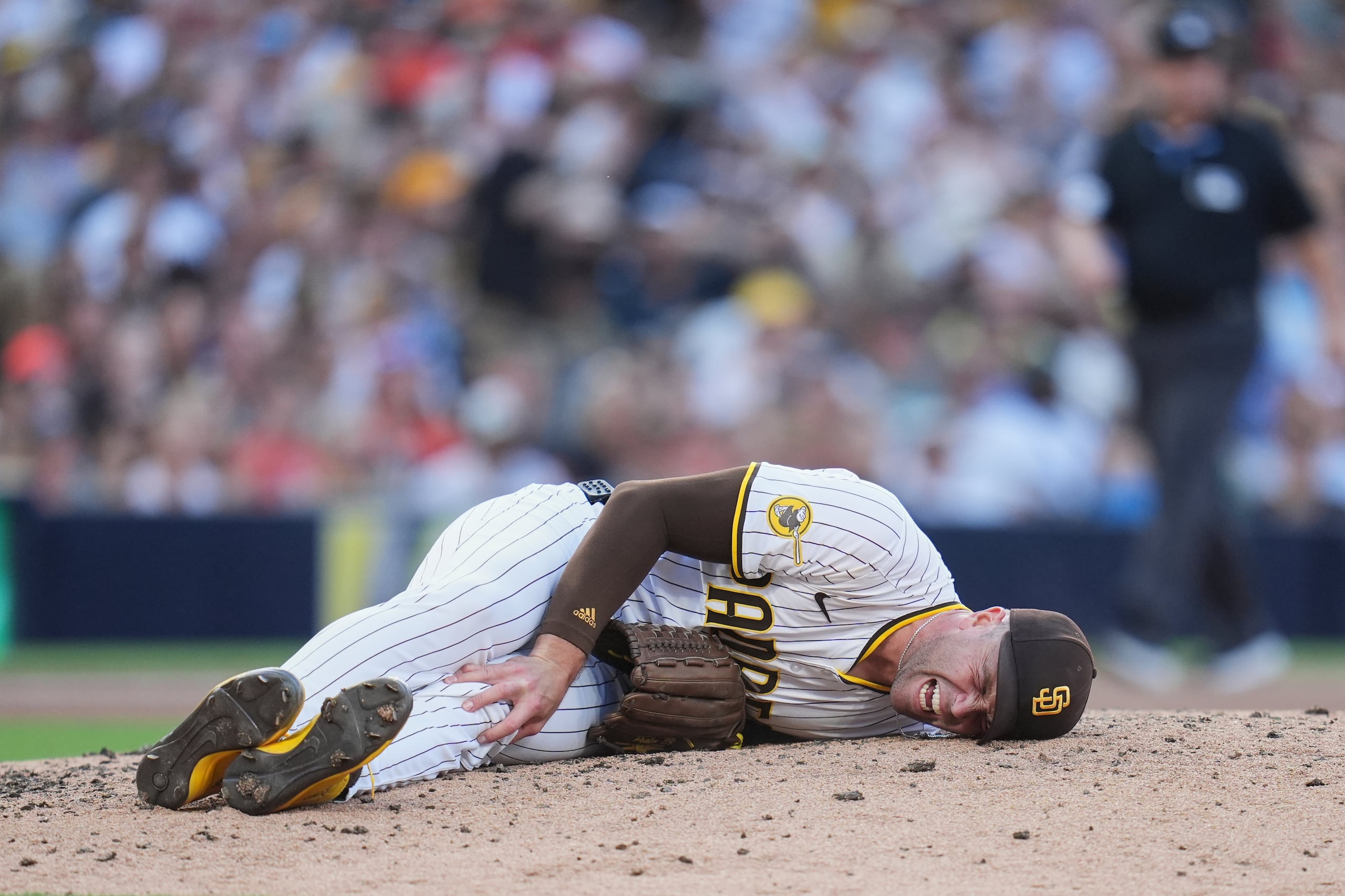 Jason Adam, relevista de los Padres de San Diego, se toma la pierna izquierda después de caer con una lesión durante la séptima entrada del juego de béisbol de Grandes Ligas contra los Orioles de Baltimore, el lunes 1 de septiembre de 2025, en San Diego. (AP Foto/Gregory Bull)