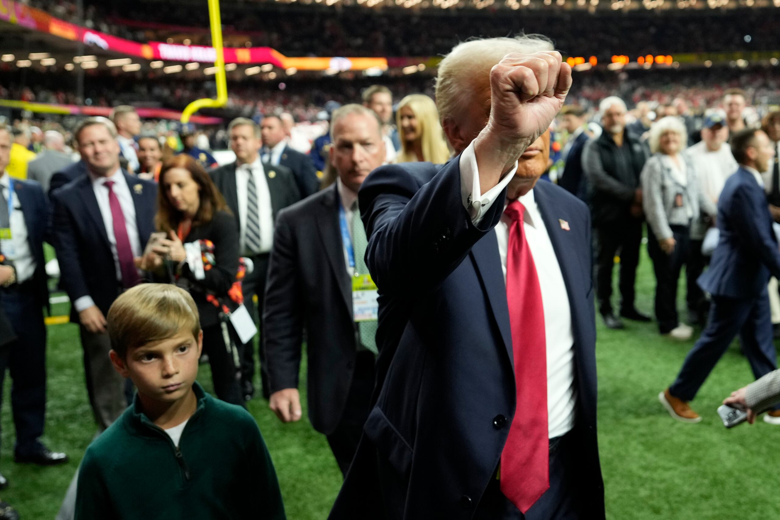 El presidente Donald Trump saluda al público mientras camina junto a su nieto Theodore antes del partido sobre el campo de juego.