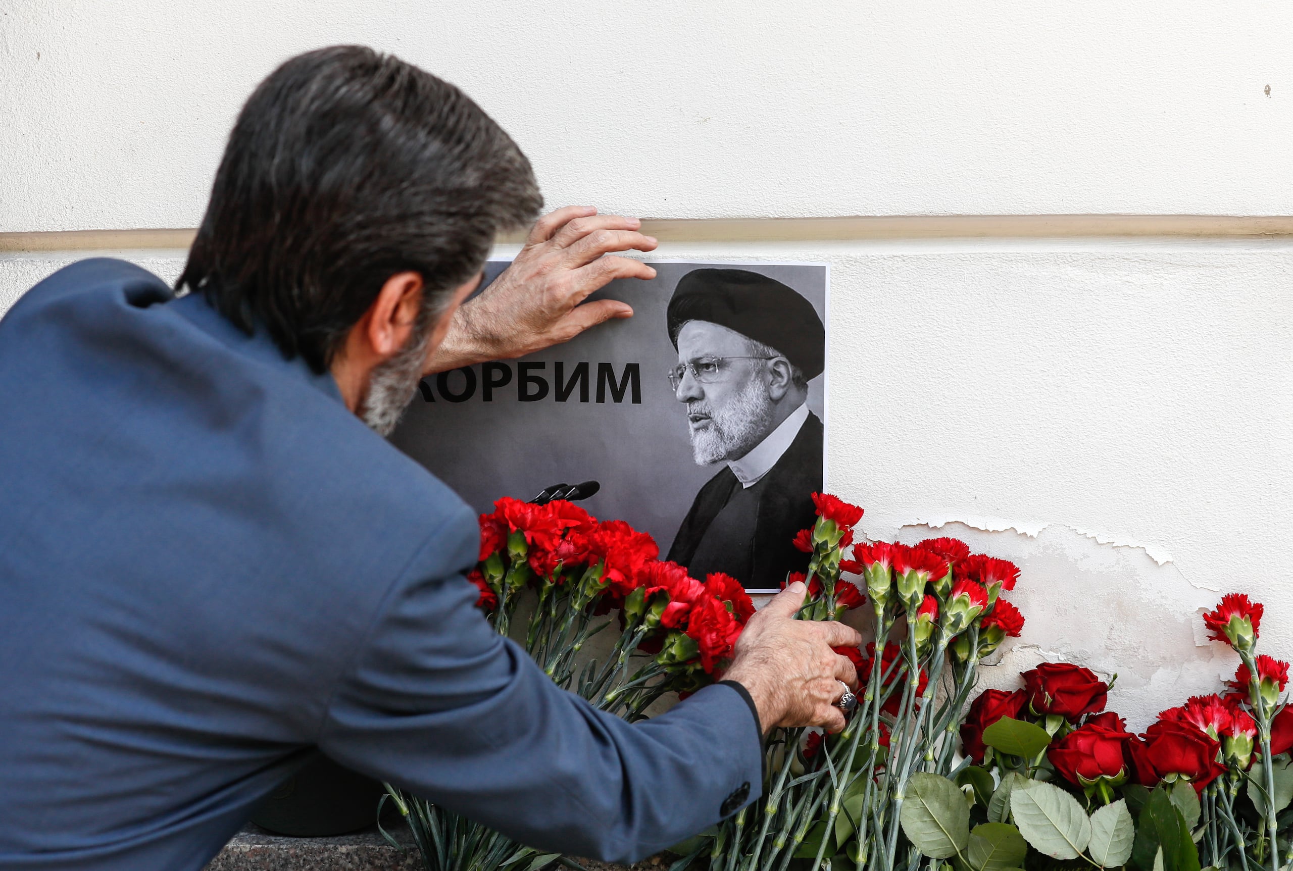 Un hombre coloca un retrato del difunto presidente iraní Ebrahim Raisi junto a flores