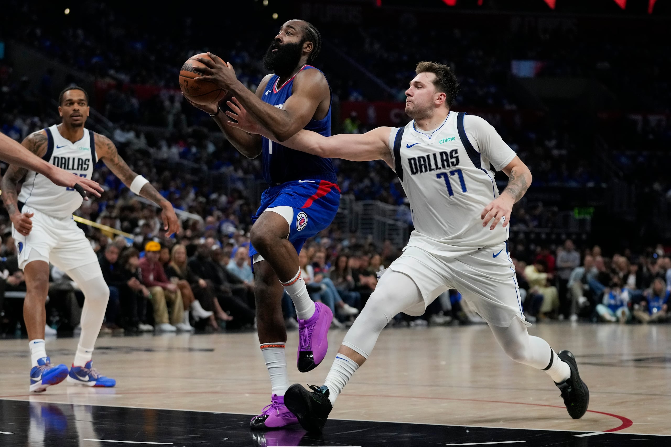Luka Doncic (77), de los Mavericks de Dallas, intenta defender una canasta de James Harden (1), de los Clippers de Los Ángeles, durante la primera mitad del Juego 1 de la serie de playoffs de primera ronda de baloncesto de la NBA, en Los Ángeles, el domingo 21 de abril de 2024. (AP Foto/Ashley Landis)