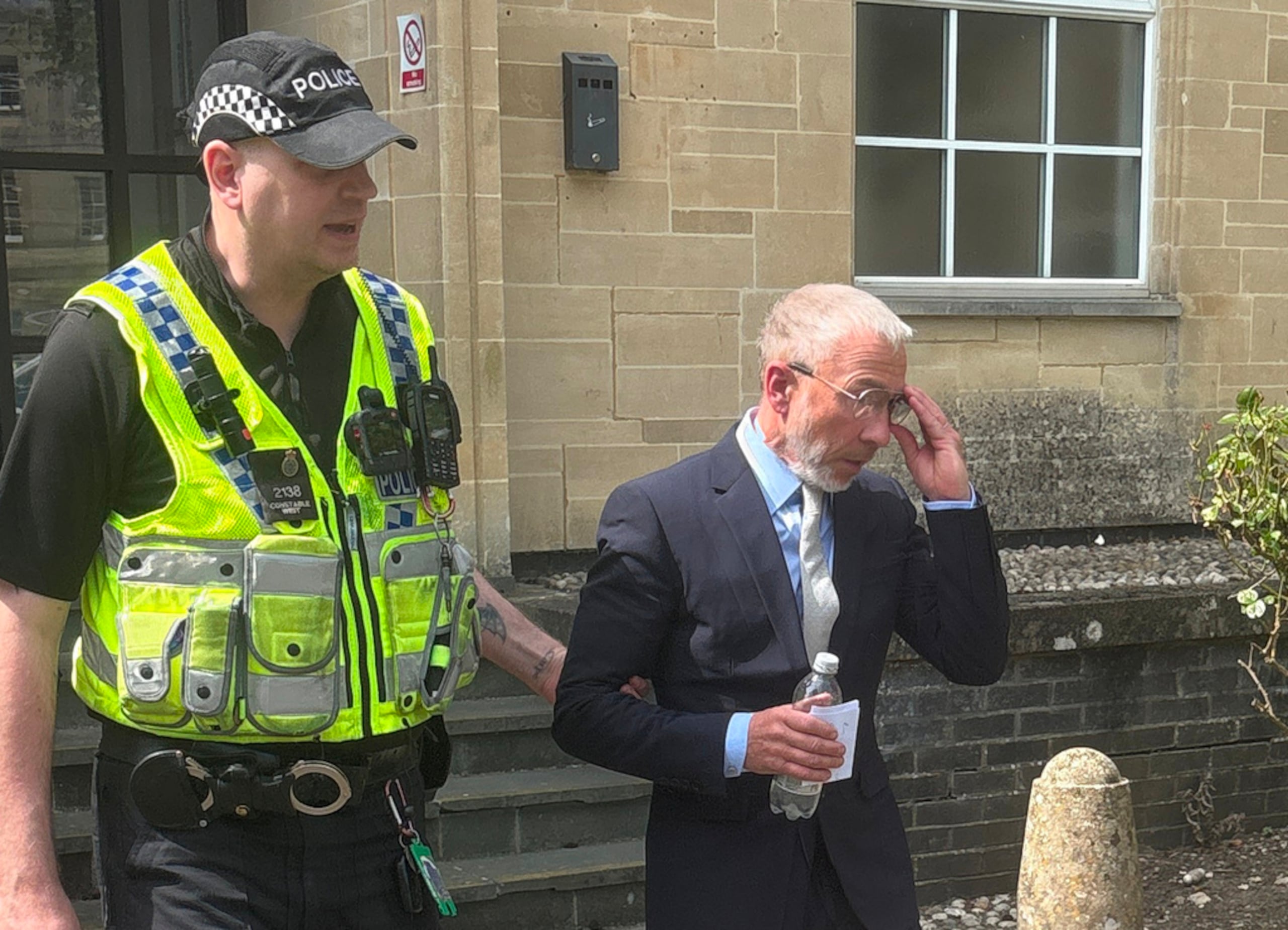 El cofundador de la empresa de ropa Superdry, James Holder, es escoltado por un agente de policía al salir del Tribunal de Magistrados de Cirencester, Inglaterra, el 1 de mayo de 2026.
