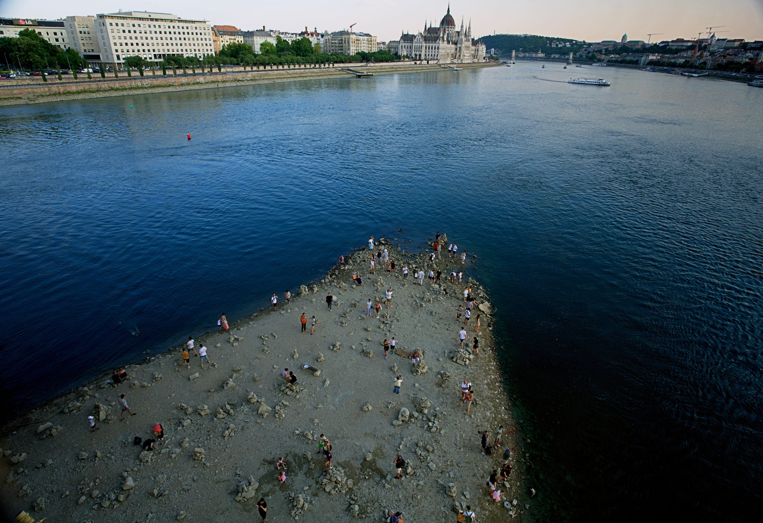 Varias personas caminan por un banco de arena bajo el puente Margarita del río Danubio, en el centro de Budapest, Hungría, mientras el río, que atraviesa 10 países europeos, ha descendido a niveles de caudal nunca vistos. (AP Foto/Bela Szandelszky)