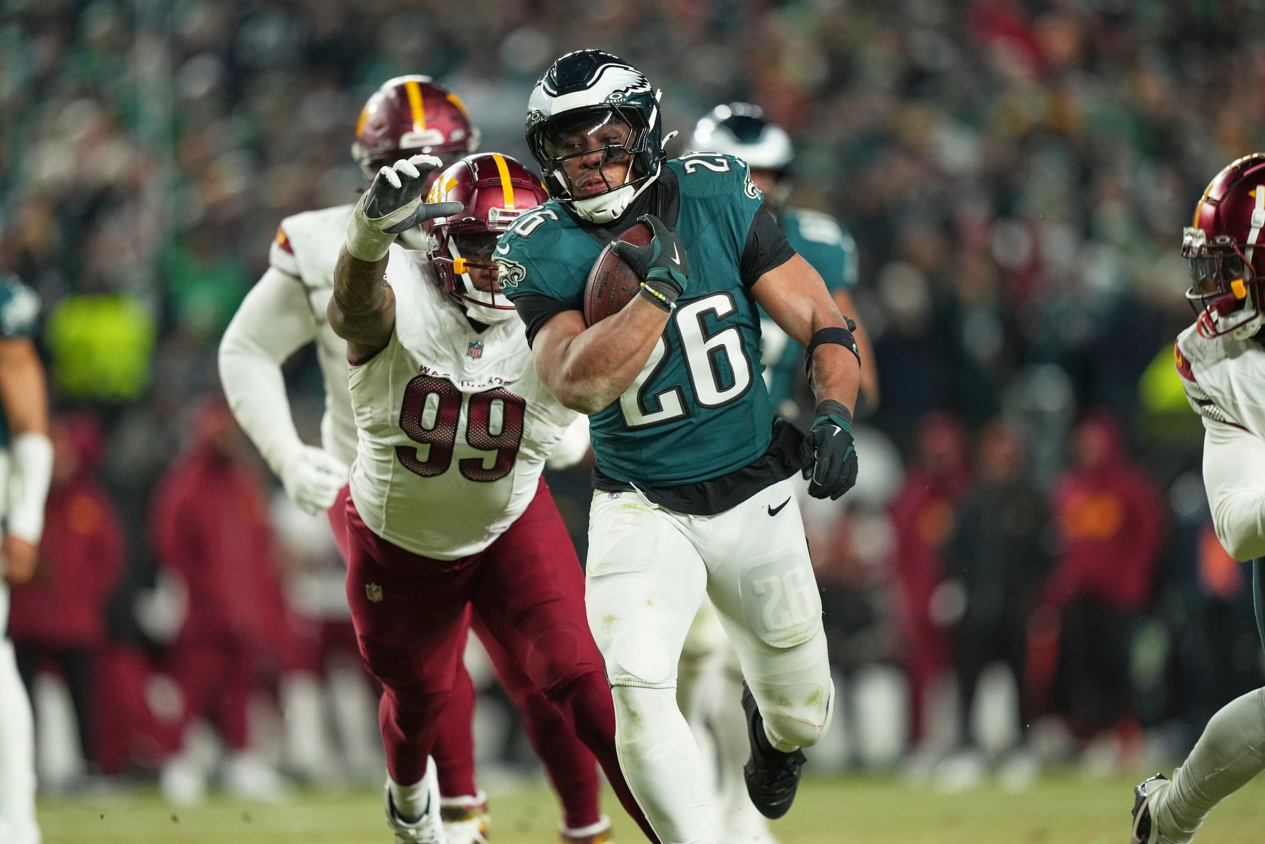 Saquon Barkley (26), running back de los Eagles de Filadelfia, corre para conseguir un primero y diez frente a los Commanders de Washington, mientras el defensive end Clelin Ferrell (99) intenta detenerlo durante la segunda mitad del Juego de Campeonato de la NFC, el domingo 26 de enero de 2025, en Filadelfia. (AP Foto/Matt Slocum)