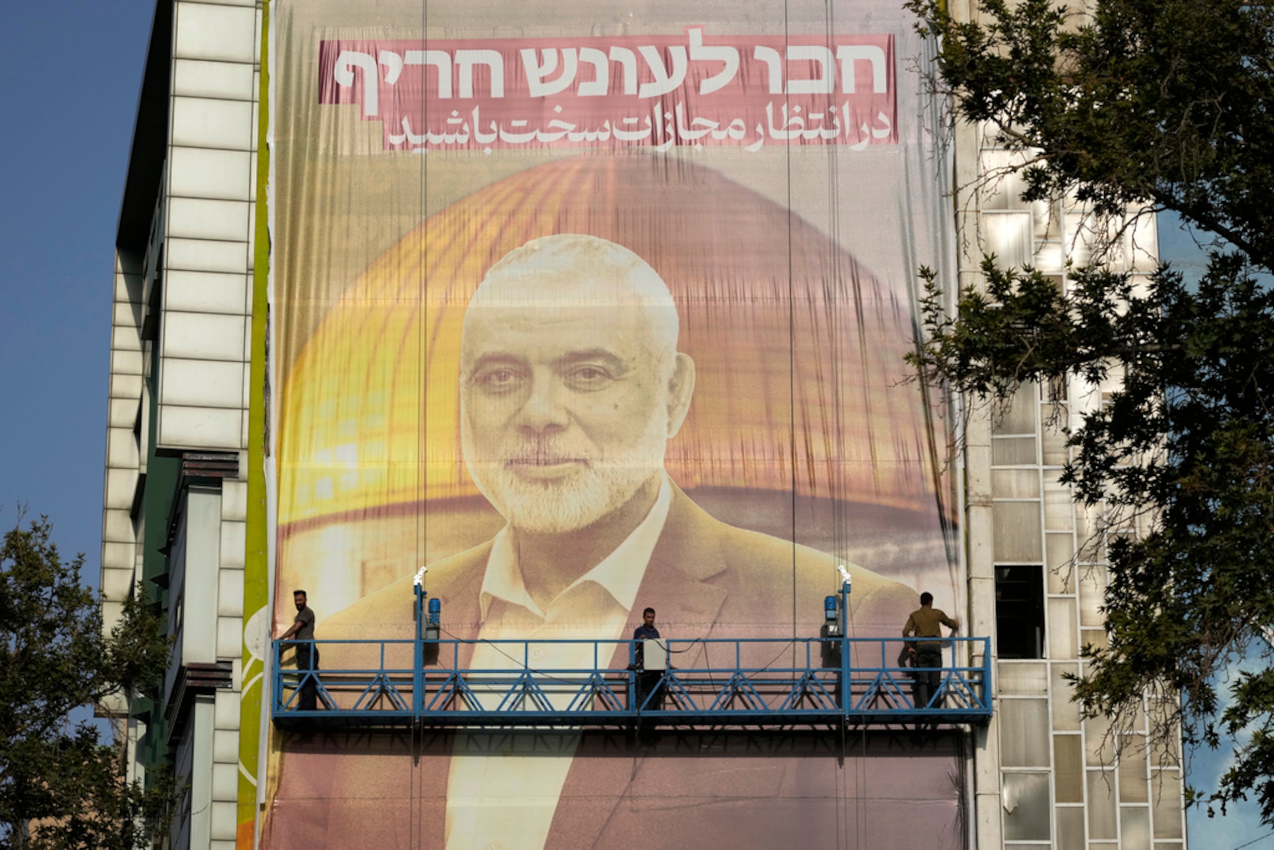 Trabajadores iraníes instalan una enorme pancarta en una pared que muestra un retrato del líder de Hamás, Ismail Haniyeh, y la Mezquita de la Cúpula de la Roca en el recinto de la Mezquita de Al-Aqsa en Jerusalén, con un cartel que dice en farsi y hebreo: "Esperen un severo castigo", en la Plaza Felestin (Palestina) en Teherán, Irán, el 31 de julio de 2024.