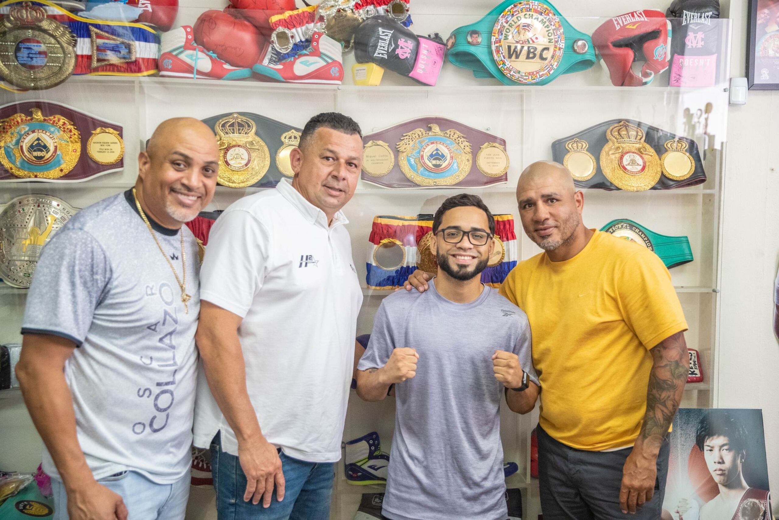 Oscar Collazo, de camisa amarilla, aparece aquí junto a su entrenador y manejador, Juan León, a la izquierda, Héctor Soto, presidente de Miguel Cotto Promotions, y del miembro del Salón de la Fama del Boxeo, Miguel Cotto, tras formalizar hoy los detalles para el pleito en San Juan el 26 de agosto. (Miguel Cotto Promotions)