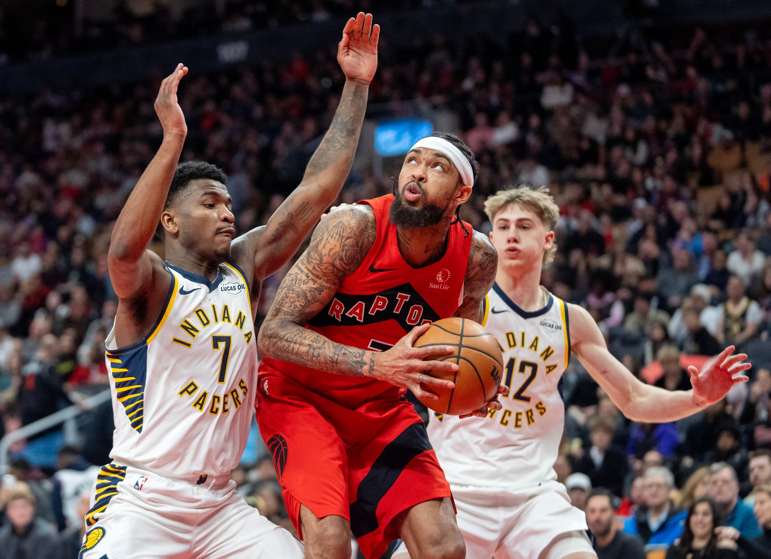 Brandon Ingram, de los Raptors de Toronto, busca avanzar al aro entre Kam Jones (7) y Johnny Furphy, de los Pacers de Indiana, el domingo 8 de febrero de 2026 (Frank Gunn/The Canadian Press via AP)
