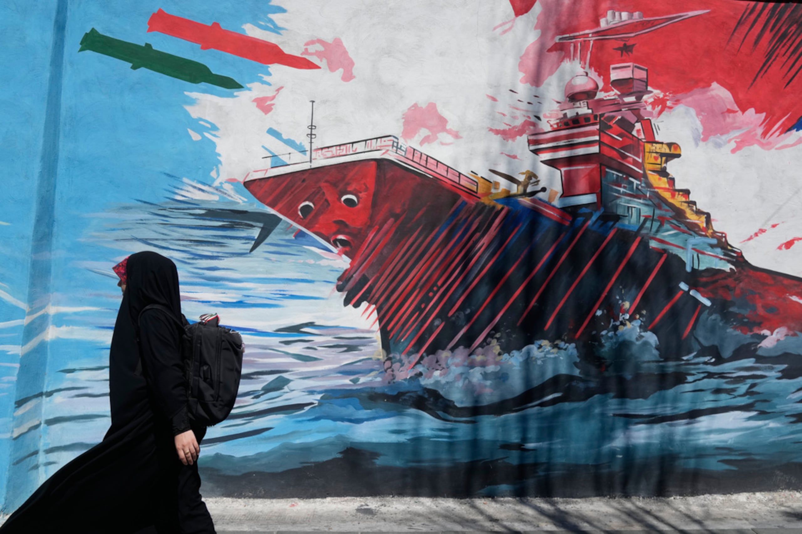 Una mujer pasa junto a un mural que muestra un portaaviones estadounidense bajo ataque en el centro de Teherán, Irán, el 8 de junio de 2026.