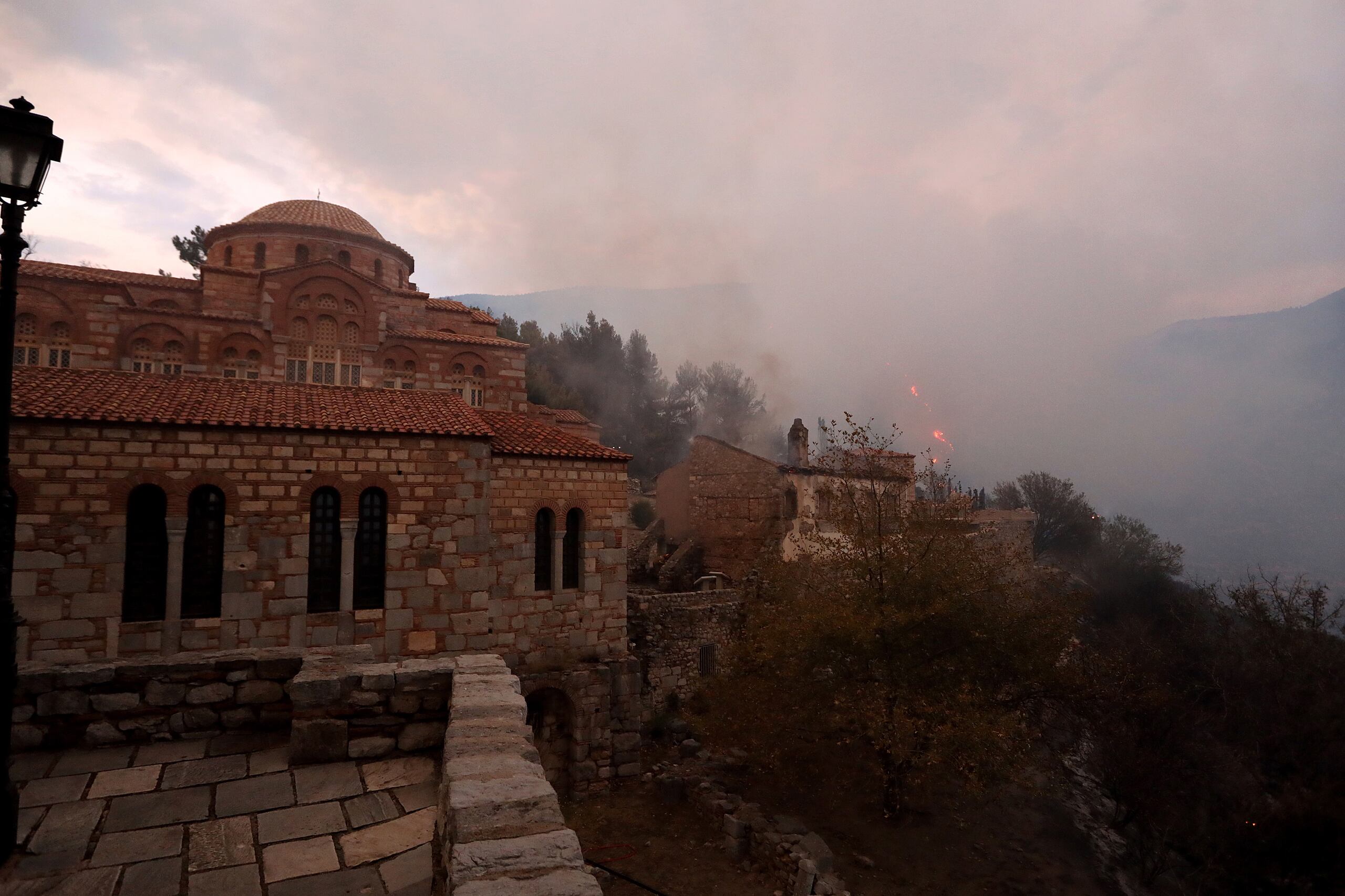 El humo del incendio se eleva desde los edificios dañados del histórico Monasterio de Hosios Loukas, que está en la Lista del Patrimonio Mundial de la UNESCO en el área de Stiri, después de que estallara un incendio forestal en Viotia, Grecia, este jueves. EFE/Pangiotis Pragiannis