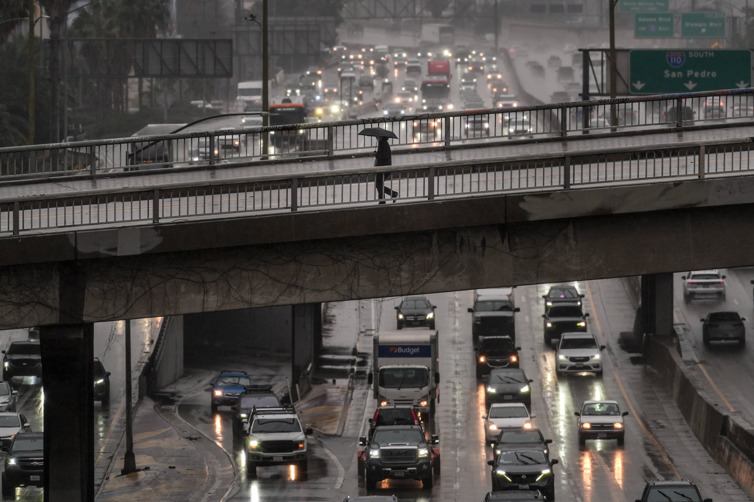 Un peatón con paraguas cruza un puente sobre la autopista 110 en medio de una tormenta.