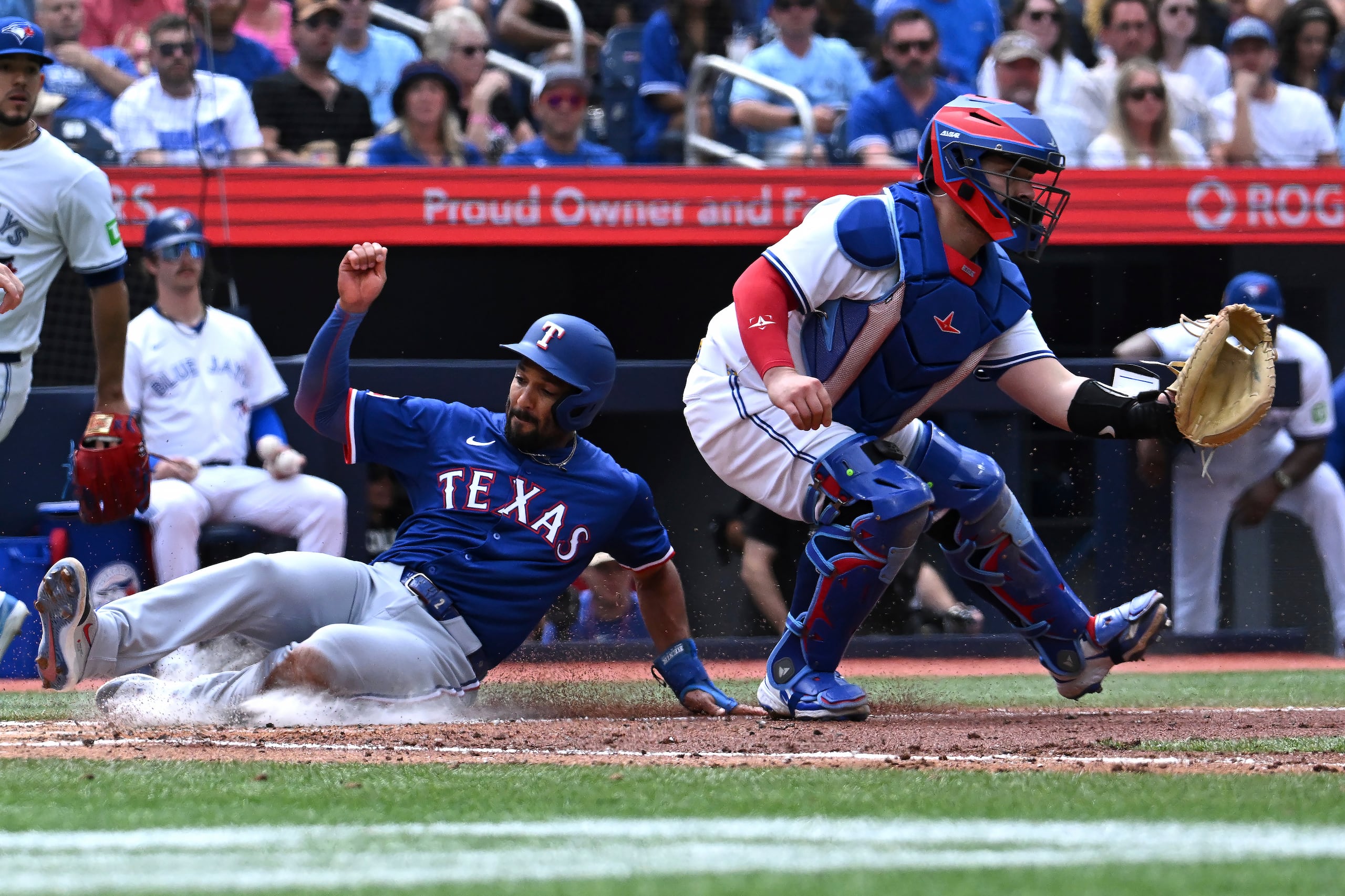 El segunda base de los Rangers de Texas Marcus Semien se desliza safe en el plato para anotar en el sencillo de Jake Burger frente al catcher de los Azulejos de Toronto Alejandro Kirk el sábado 17 de agosto del 2025. (Jon Blacker/The Canadian Press via AP)