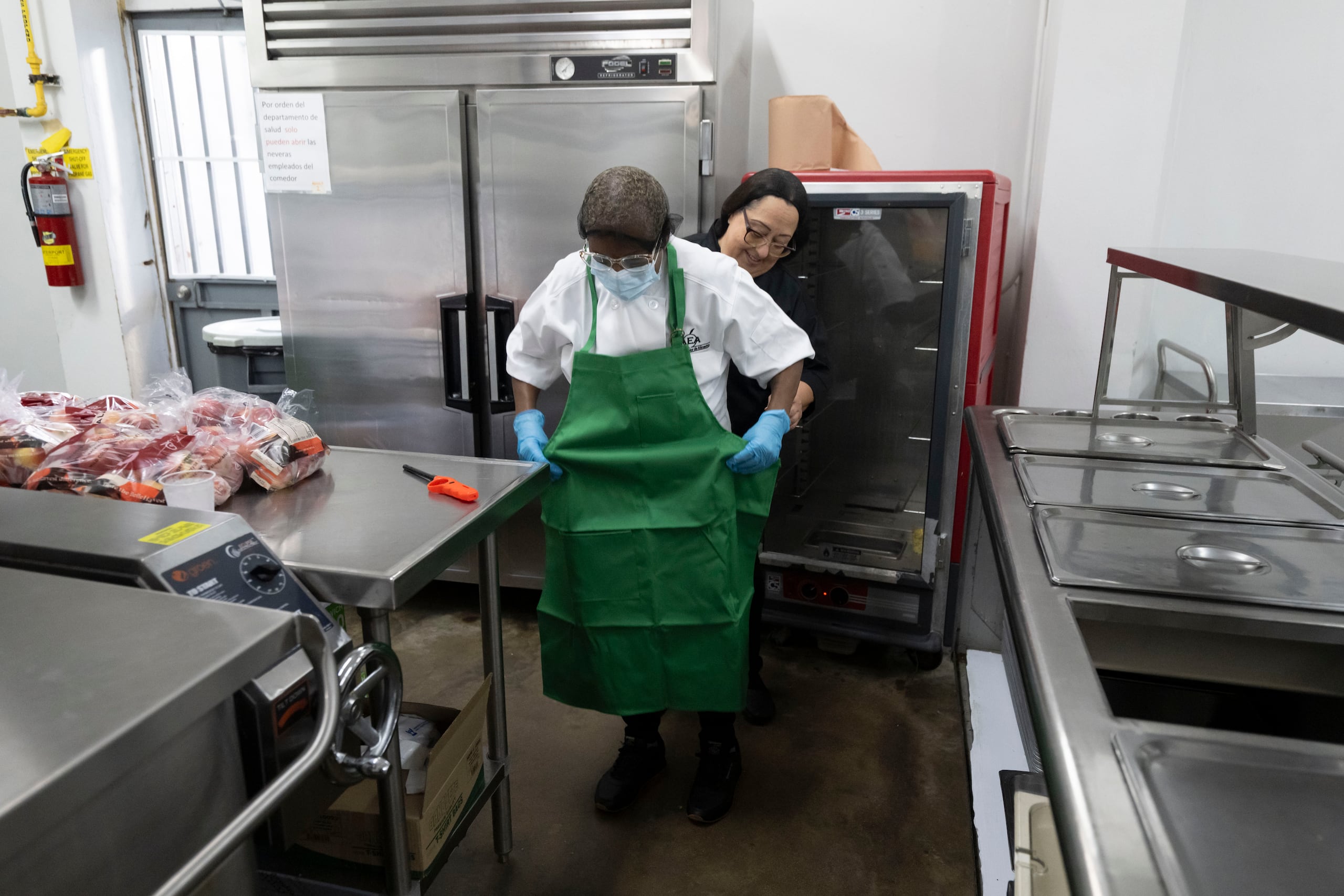 Lilliam Domena, encargada del comedor escolar de la escuela José Celso Barbosa, en Puerta de Tierra, ayuda a Nitza Carrasquillo a ponerse el delantar. FOTO POR: Carlos Rivera Giusti/GFR Media