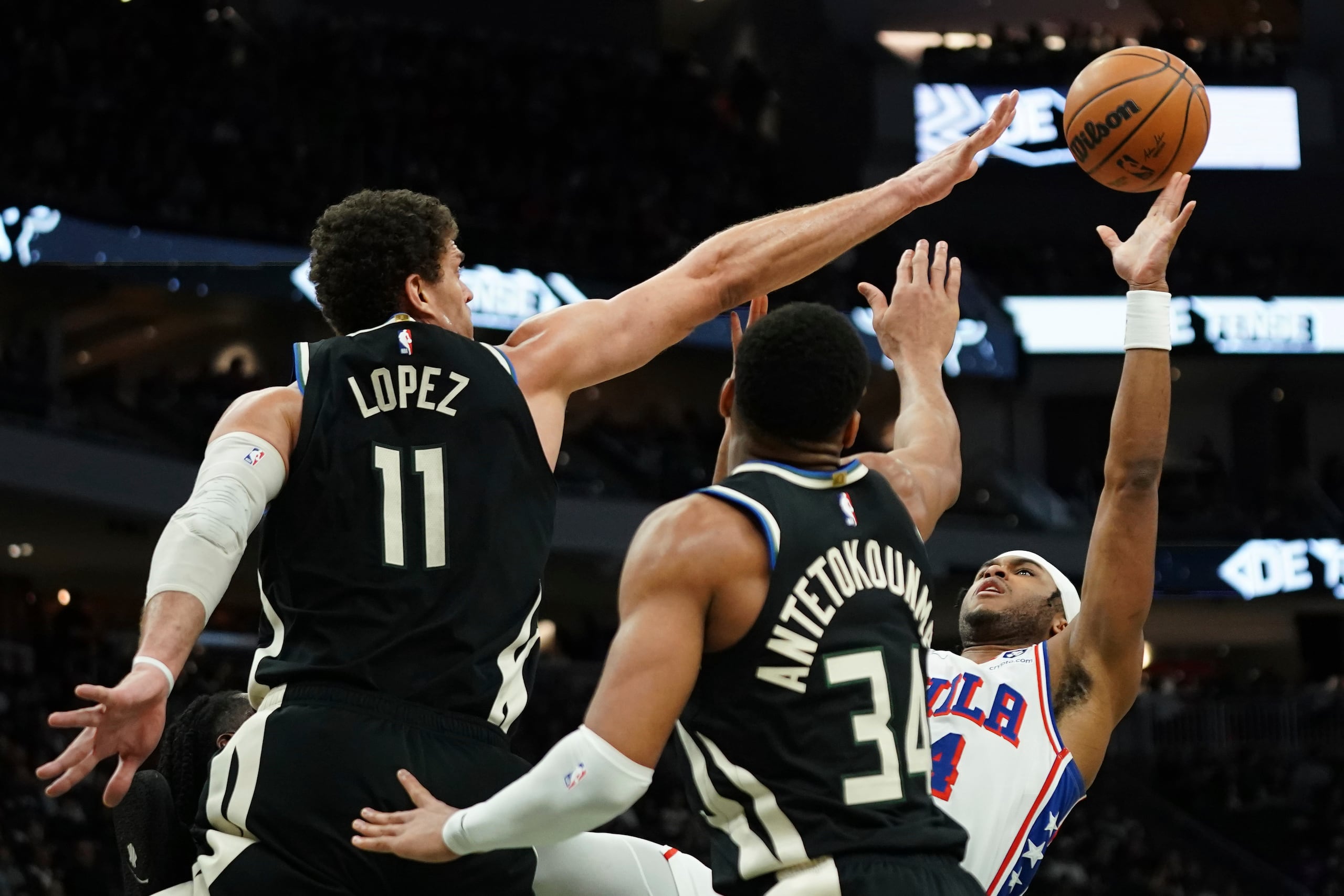 Ricky Council IV, de los 76ers de Filadelfia, a la derecha, dispara alrededor de Brook López (11) y Giannis Antetokounmpo (34), de los Bucks de Milwaukee, durante la primera mitad de un partido de baloncesto de la NBA, el domingo 19 de enero de 2025, en Milwaukee. (AP Foto/Aaron Gash)