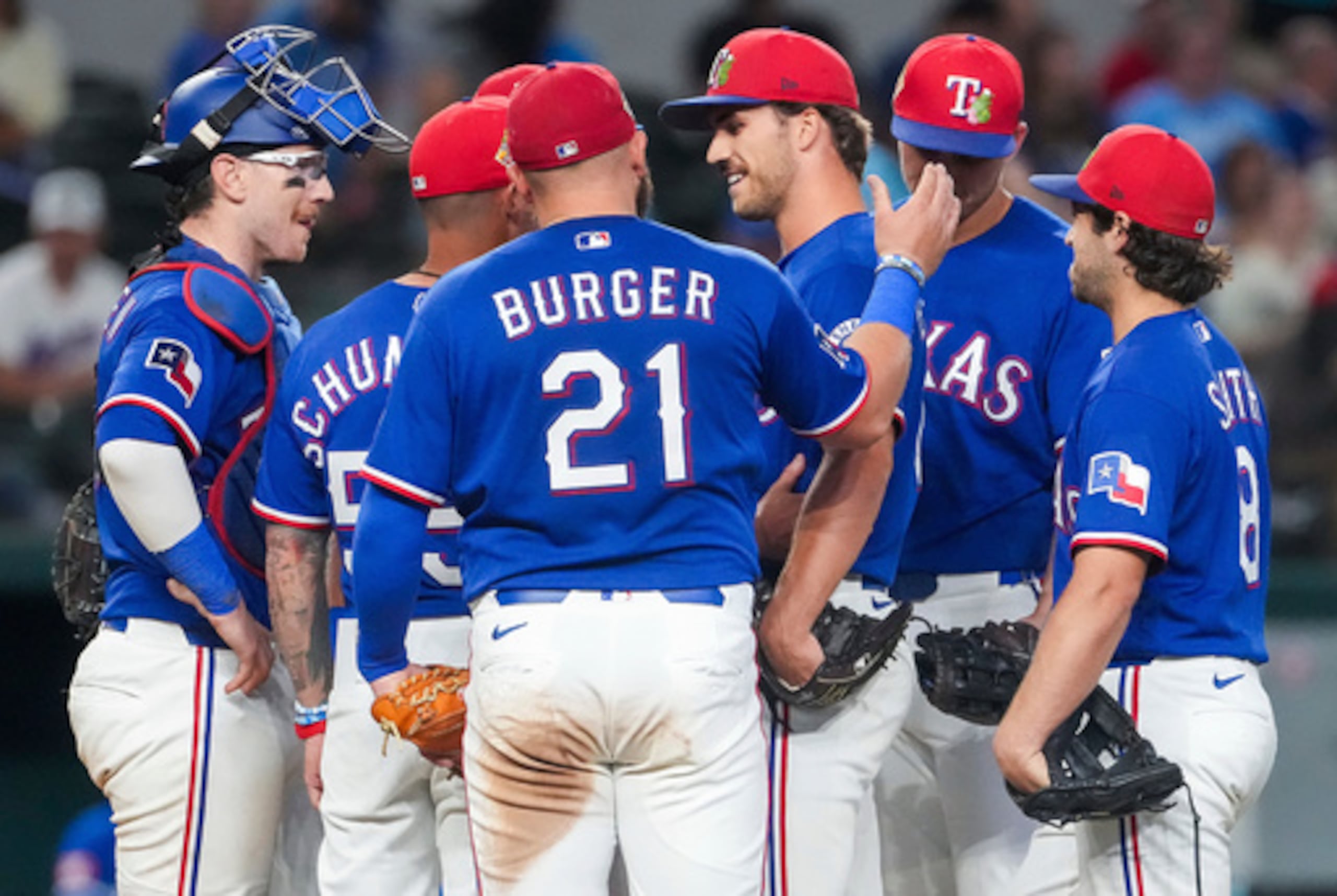 El lanzador de los Rangers de Texas Carter Baumler, tercero desde la derecha, recibe una palmada en la espalda del primera base Jake Burger (21) mientras recibe la visita en el montículo del manager Skip Schumaker, segundo desde la izquierda, para informarle que ha entrado en la lista del día de apertura durante la quinta entrada de un partido de béisbol de exhibición contra los Reales de Kansas City, el lunes 23 de marzo de 2026, en Arlington, Texas. (Smiley N. Pool/The Dallas Morning News vía AP)