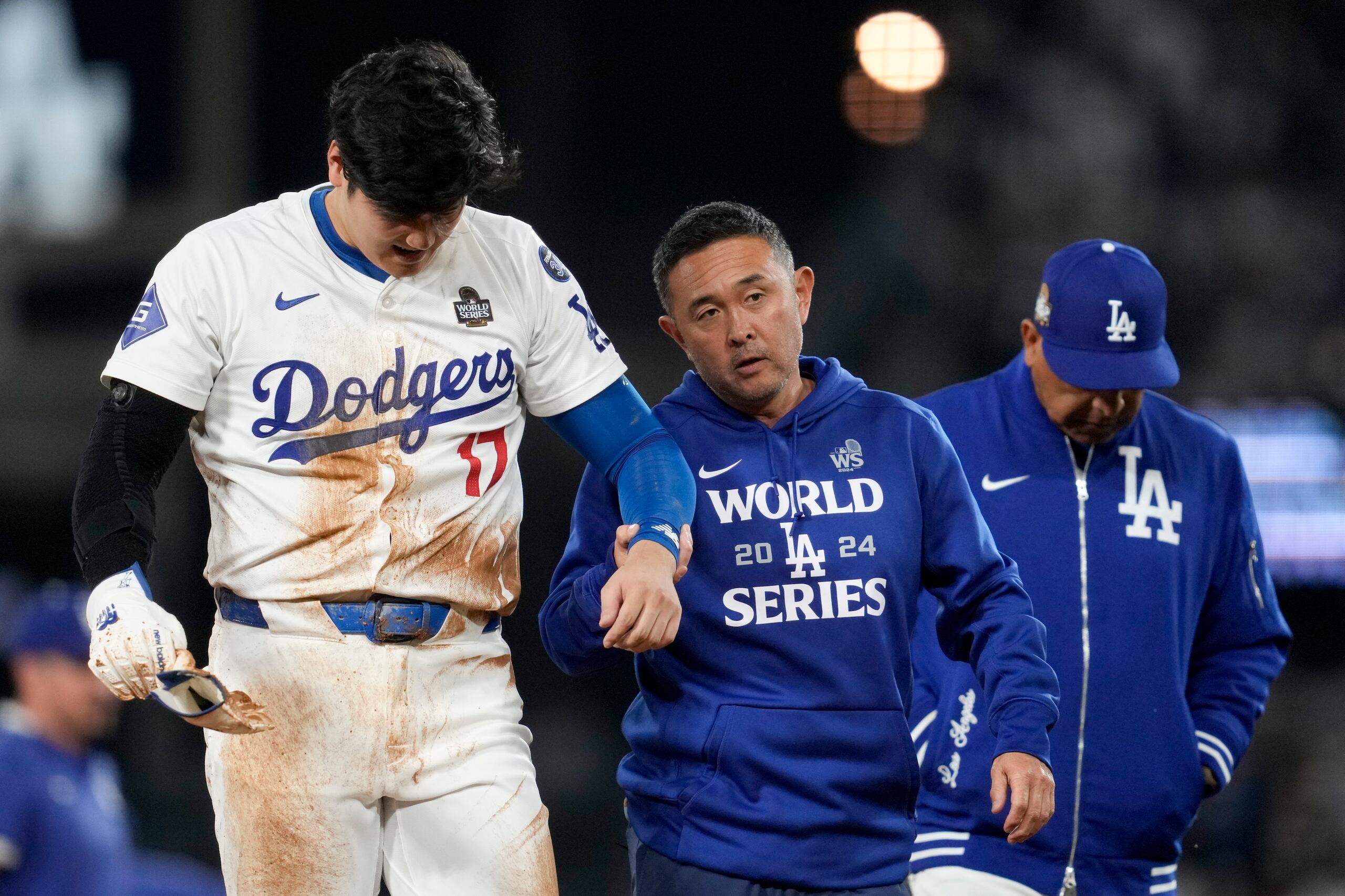 Shohei Ohtani, de los Dodgers de Los Ángeles, es asistido en su salida del terreno después de lesionarse el hombro izquierdo en la séptima entrada del segundo juego de la Serie Mundial.