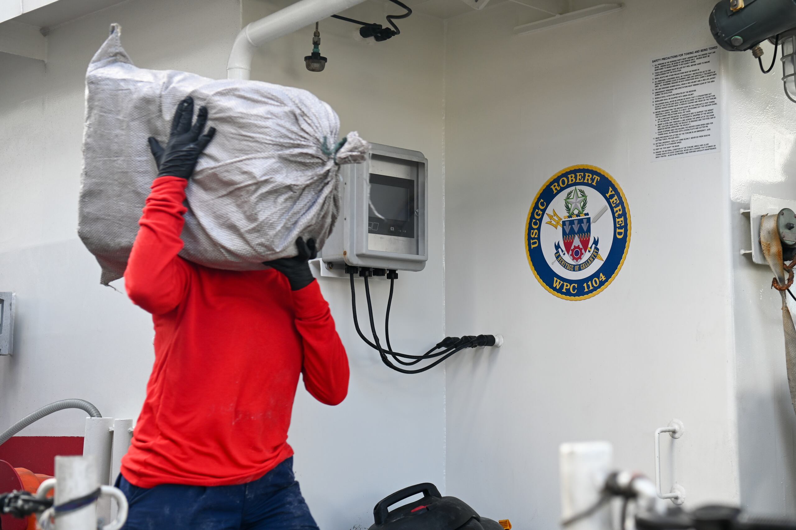 Fotografía cedida por la Guardia Costera de Estados Unidos de un hombre mientras descarga un paquete de cocaína que pertenece a un cargamento decomisado en un operativo en el Caribe. (EFE/Nicholas Strasburg/Guardia Costera EEUU)