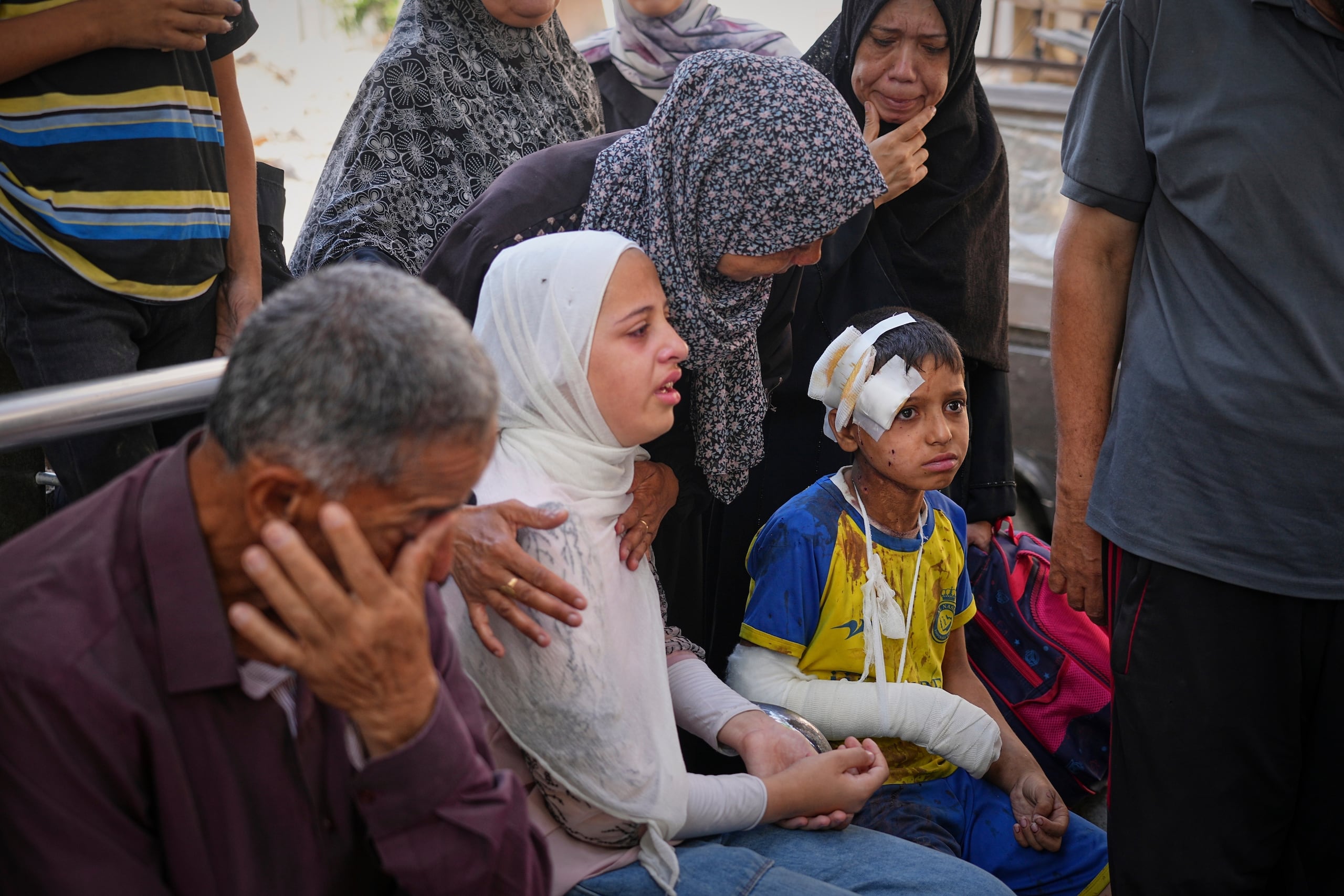 Hamam Al-Farani, sentado junto a su hermana (de blanco) y otros familiares, mientras preparan el cadáver de su padre, Alaa, que murió en un ataque israelí que causó lesiones al menor, para su entierro, en el hospital de Shifa, en Ciudad de Gaza, el 24 de junio de 2025. (AP Foto/Jehad Alshrafi)