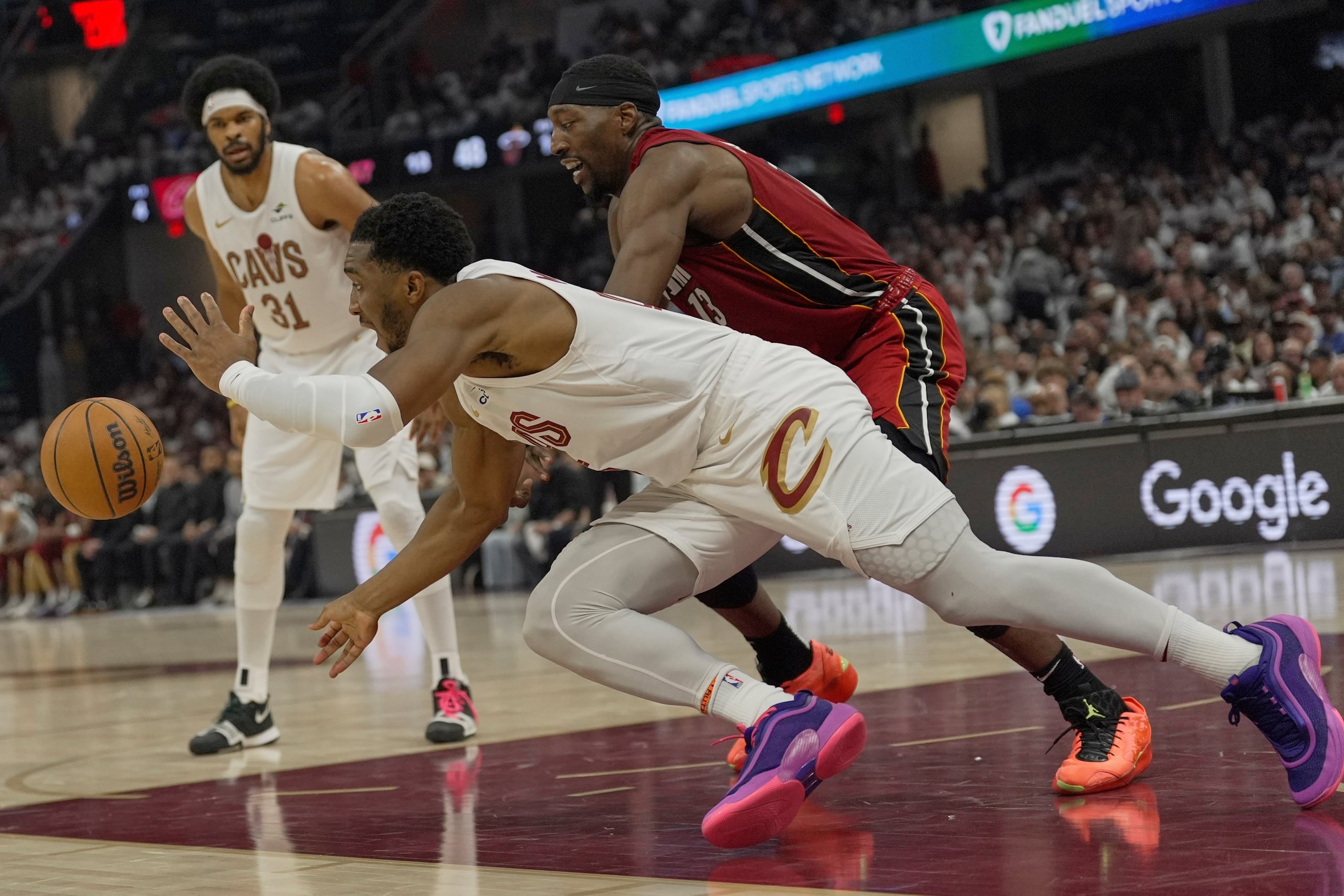 Donovan Mitchell, al frente, de los Cavaliers de Cleveland, y Bam Adebayo, derecha, del Heat de Miami, buscan controlar un balón suelto en la primera mitad del juego 1 de la serie de playoffs de la NBA, el domingo 20 de abril de 2025, en Cleveland. (AP Foto/Sue Ogrocki)