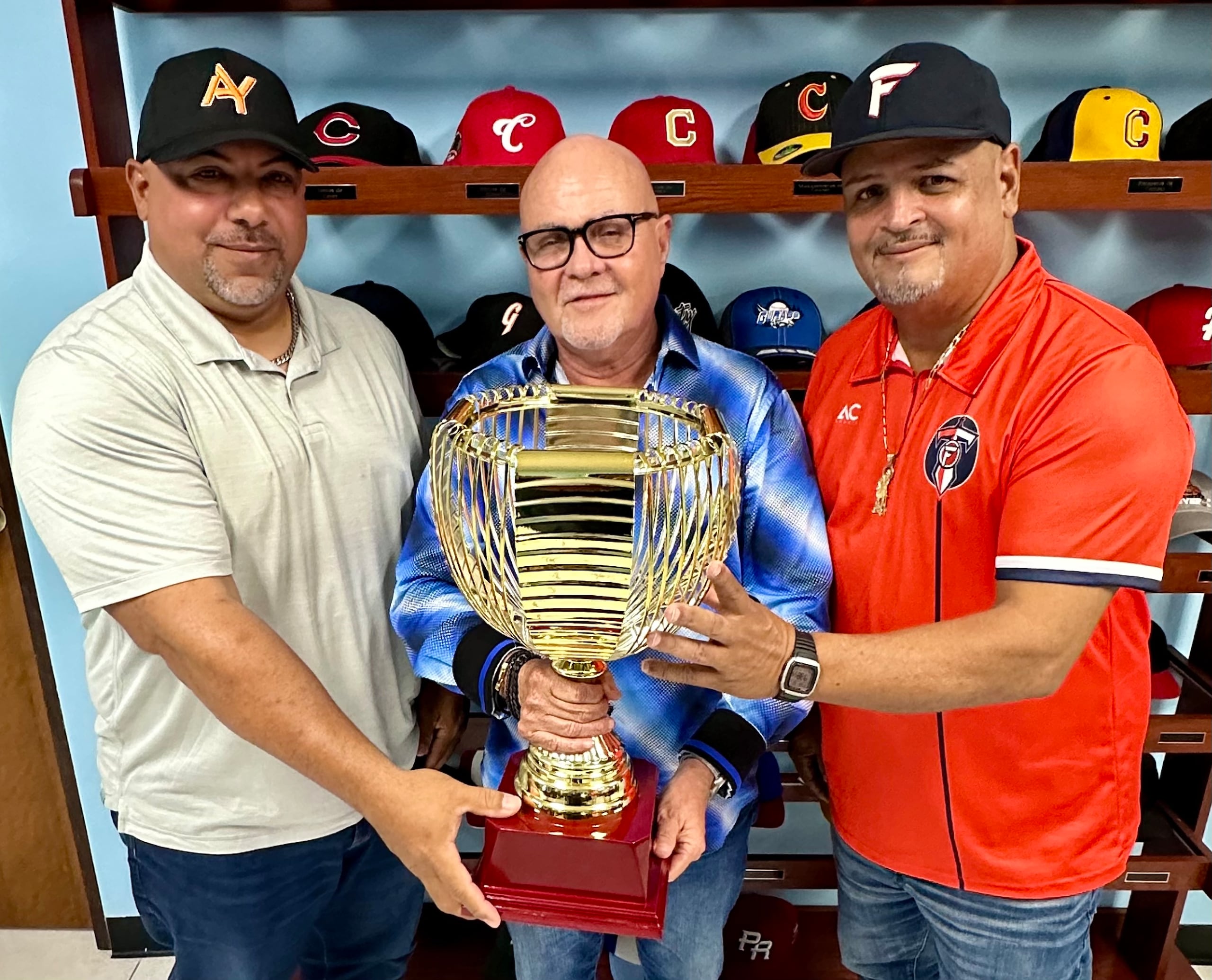 El presidente de la Federación de Béisbol, Dr. José Quiles, muestra el trofeo de campeón a los dirigentes de los Azucareros de Yabucoa y los Titanes de Florida.