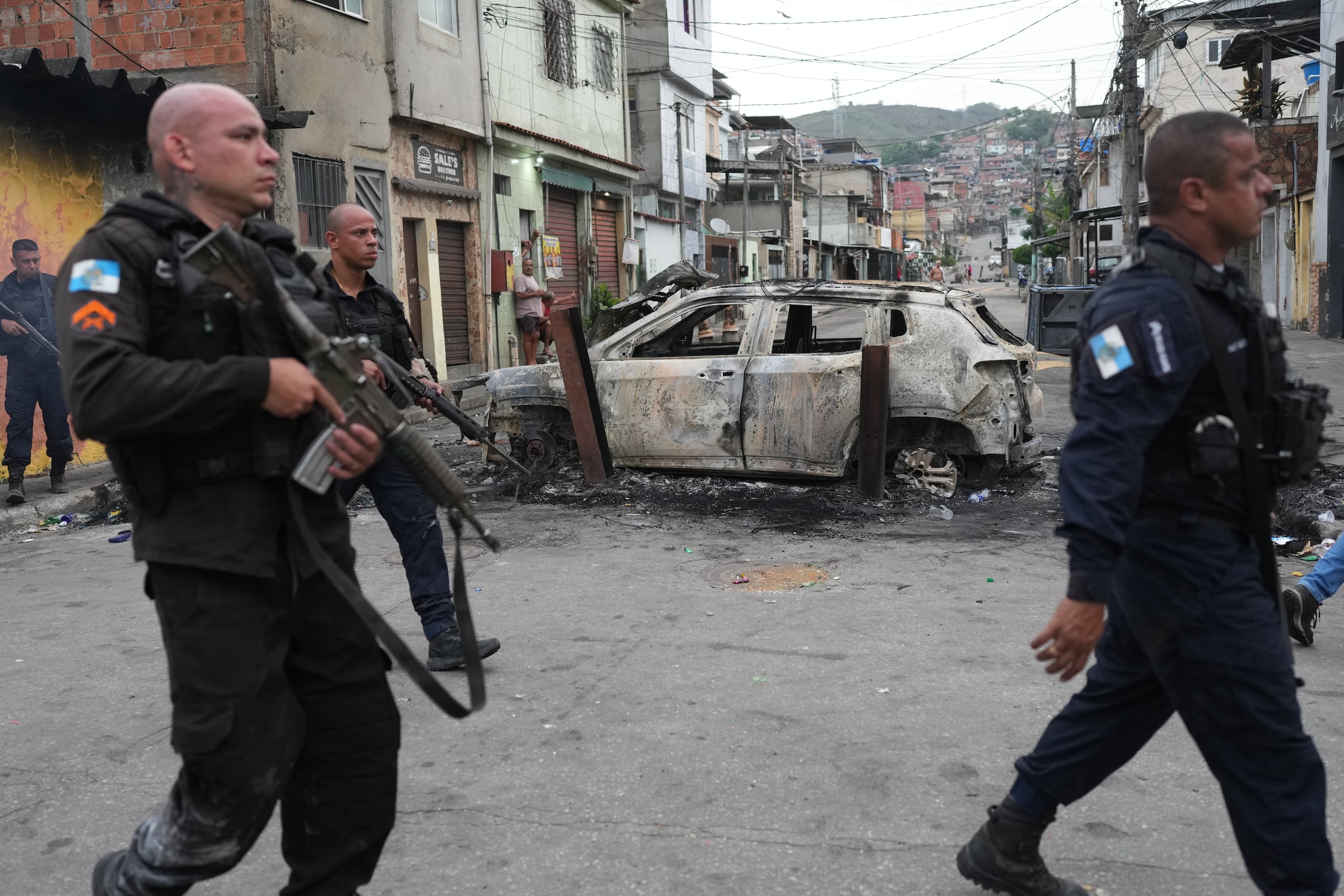 Policías pasan junto a un coche quemado que fue utilizado como barricada durante una operación policial contra presuntos narcotraficantes en la favela Complexo do Alemao, donde opera la organización criminal "Comando Vermelho", en Río de Janeiro, el martes 28 de octubre de 2025. (AP Foto/Silvia Izquierdo)