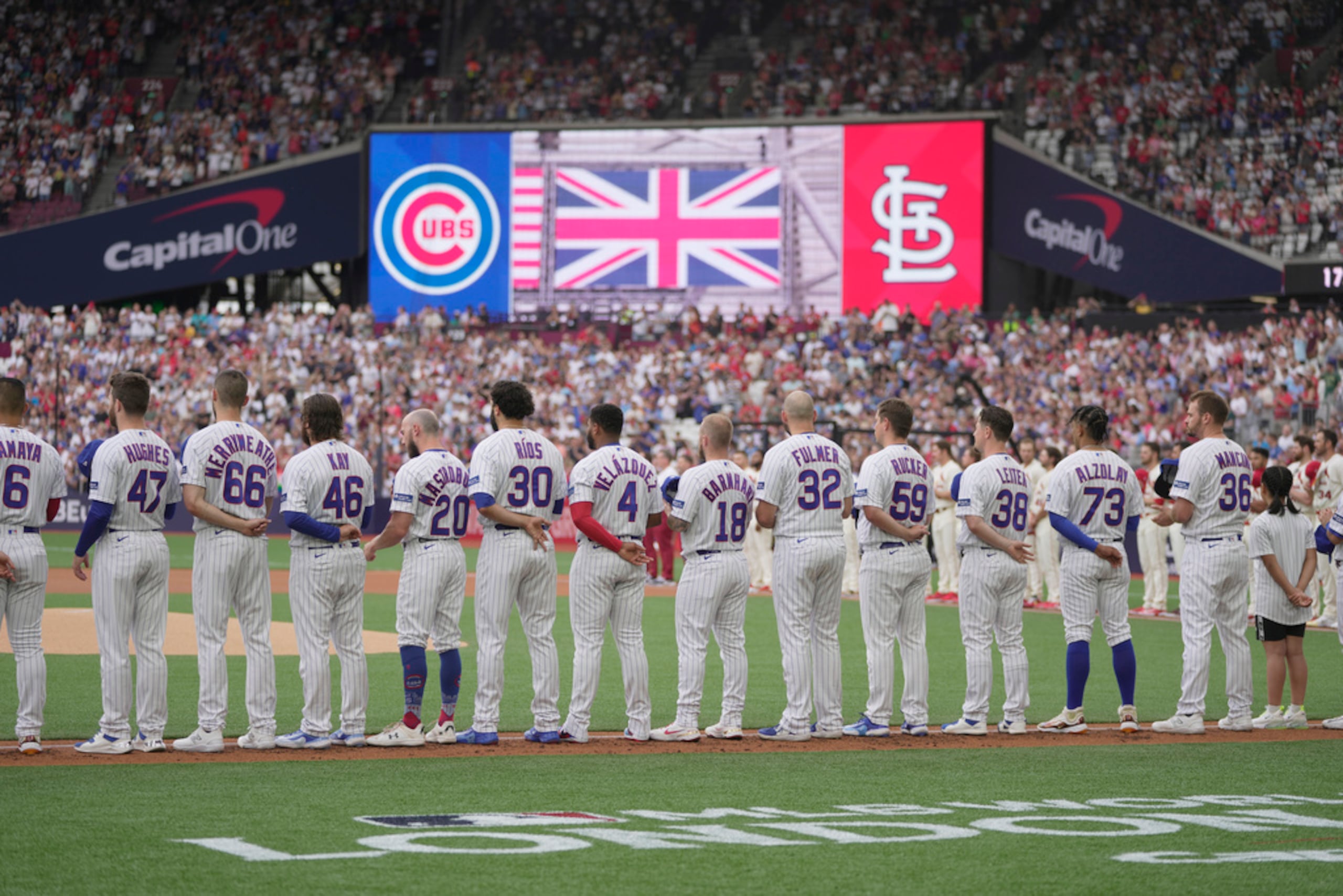 Jugadores de los Cubs de Chicago se alinean durante la ceremonia de los himnos de Estados Unidos e Inglaterra previo al partido de béisbol en contra de los Cardinals de San Luis.