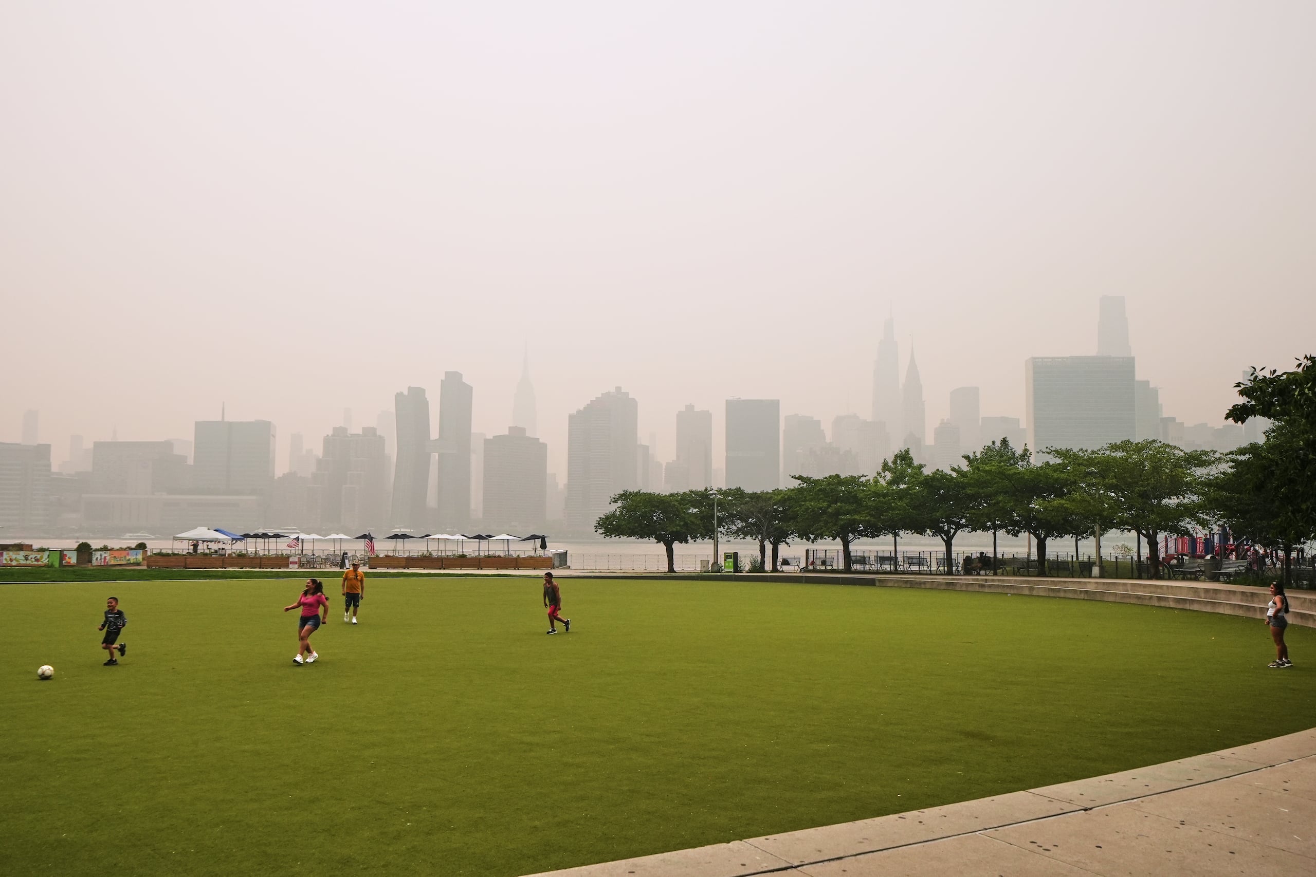 Un grupo de personas juega en el Hunter's Point South Park Athletic Field. Al fondo se aprecian los rascacielos de Nueva York, ocultos parcialmente por el humo de los incendios forestales en Canadá, el jueves 16 de julio de 2026.