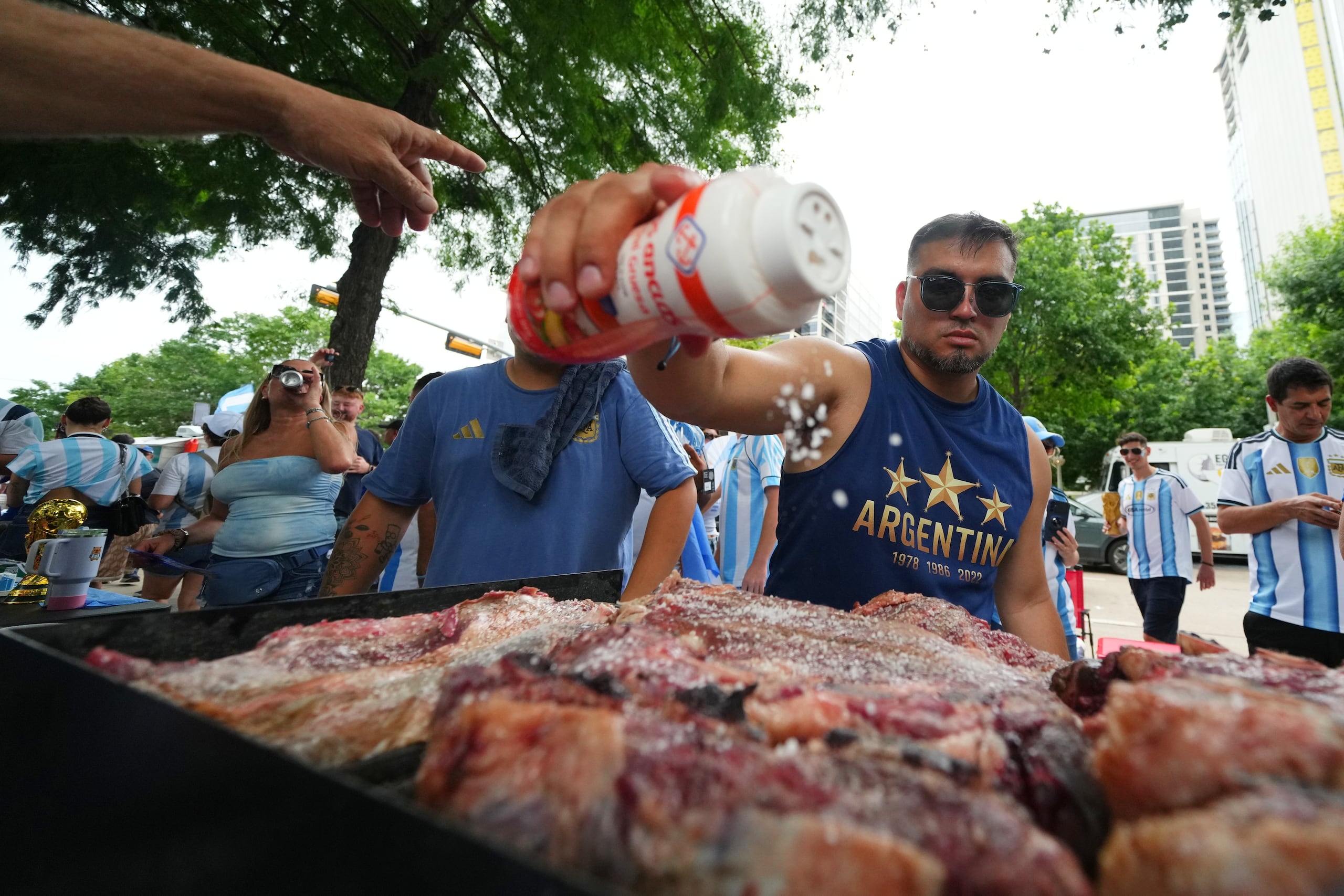 El hincha Lucas Martínez adoba las carnes con sal al preparar un asado previo al partido entre Argentina y Austria en el Mundial, el domingo 21 de junio de 2026, en Dallas. (AP Foto/Julio Cortez)