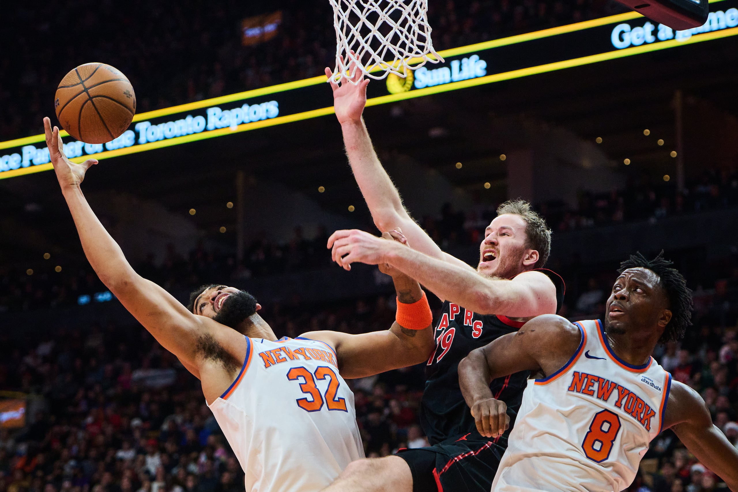 Jakob Poeltl de los Raptors de Toronto pelea por el balón en la canasta con Karl-Anthony Towns y OG Anunoby de los Knicks de Nueva York en el encuentro de cuartos de final de la Copa de la NBA el mates 9 de diciembre del 2025. (Sammy Kogan/The Canadian Press via AP)