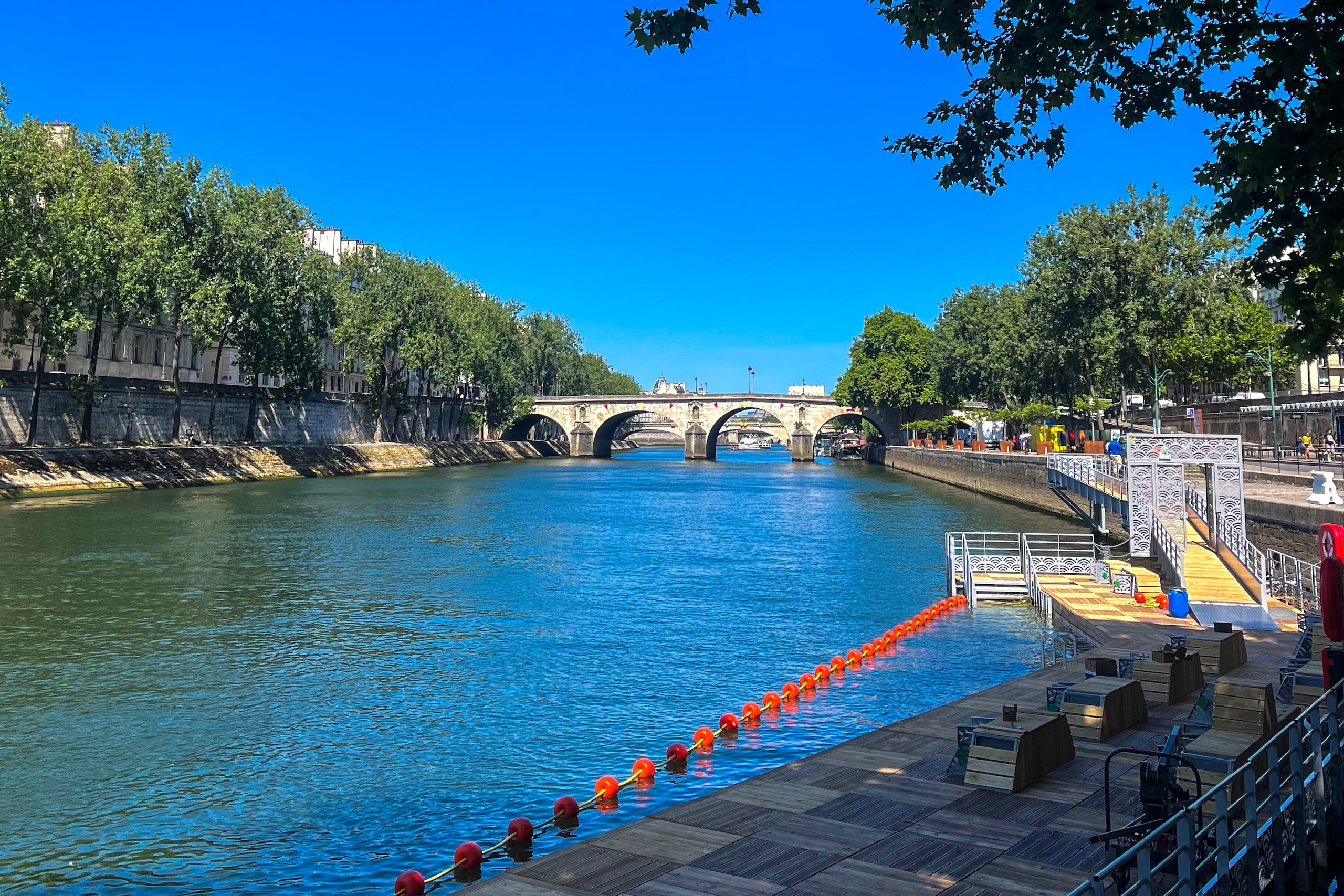 Las plataformas de madera y las boyas naranjas que conforman la nueva zona de baño en el río Sena en Bras Marie frente la Isla Saint-Louis, entre el puente Sully y el puente Marie (al fondo). Este es uno de los tres espacios habilitados para nadar en el Sena que abrirán mañana como herencia de los trabajos de mejora fluvial tras los Juegos Olímpicos 2024.-EFE/ Val Torres